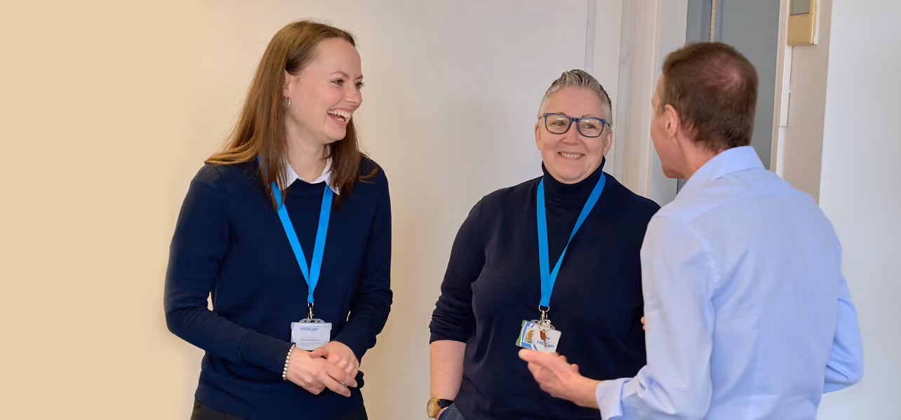 Three Fedcap colleagues wearing blue lanyards talk together in an office hallway.