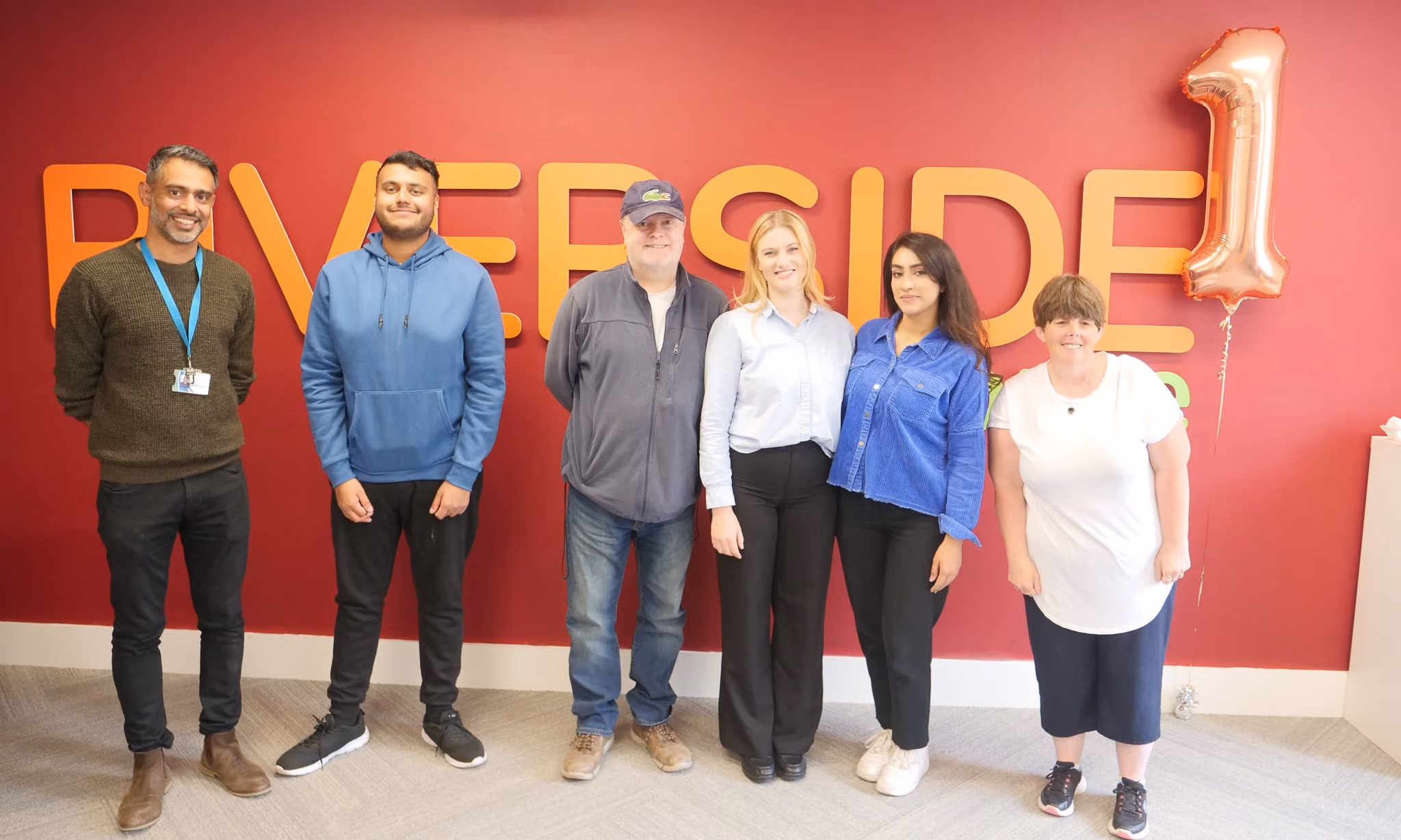Six Fedcap colleagues pose together in front of large “RIVERSIDE” lettering and a number “1” balloon.