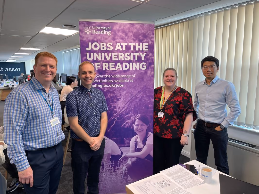 Four colleagues pose together at the University of Reading beside a “Jobs at the University of Reading” banner.