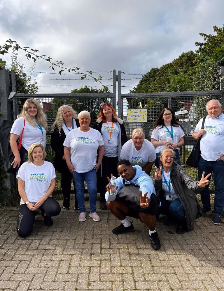 A large group of Fedcap Inspire staff in matching white t-shirts pose together outdoors.