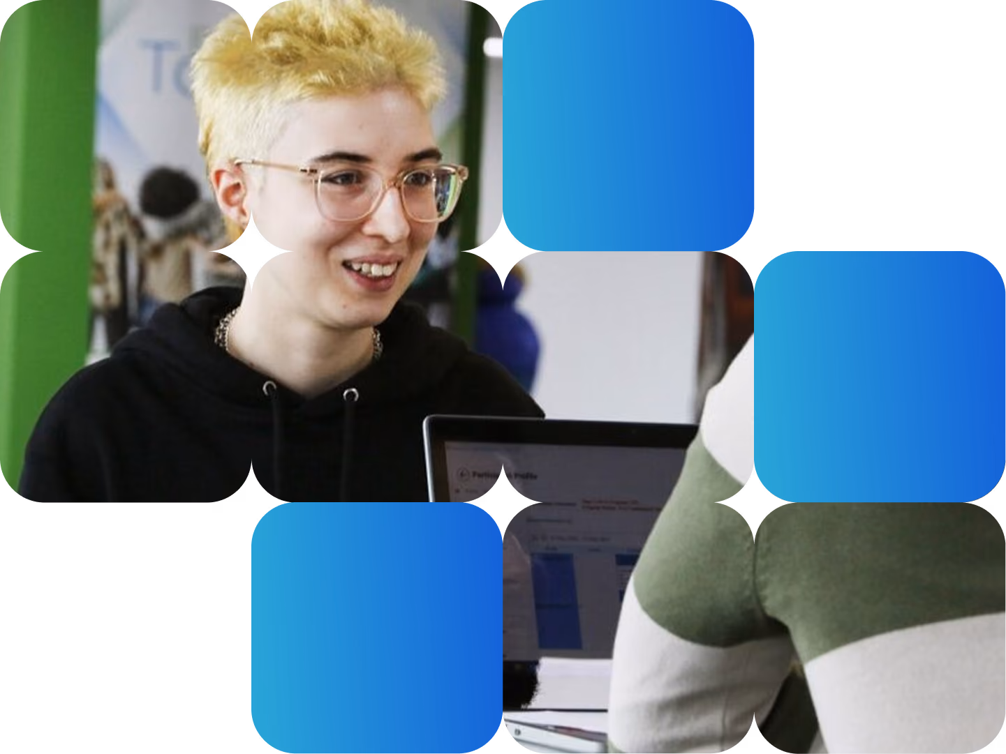 A young person with short blonde hair and glasses smiles while talking with someone across a laptop.