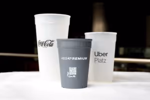 Three branded cups on a white surface: Coca-Cola, Aero Premium, and Uber Platz.