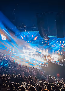 Crowded concert with bright blue stage lights and large speakers in a dark indoor venue.