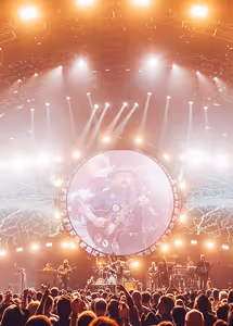 Crowd watching a concert with bright stage lights and a circular screen showing a musician playing guitar.