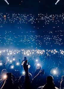Crowd at concert holding phones with flashlights on in a dark venue.
