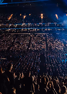 Large crowd at a concert or event with stage lighting in a dark indoor arena.