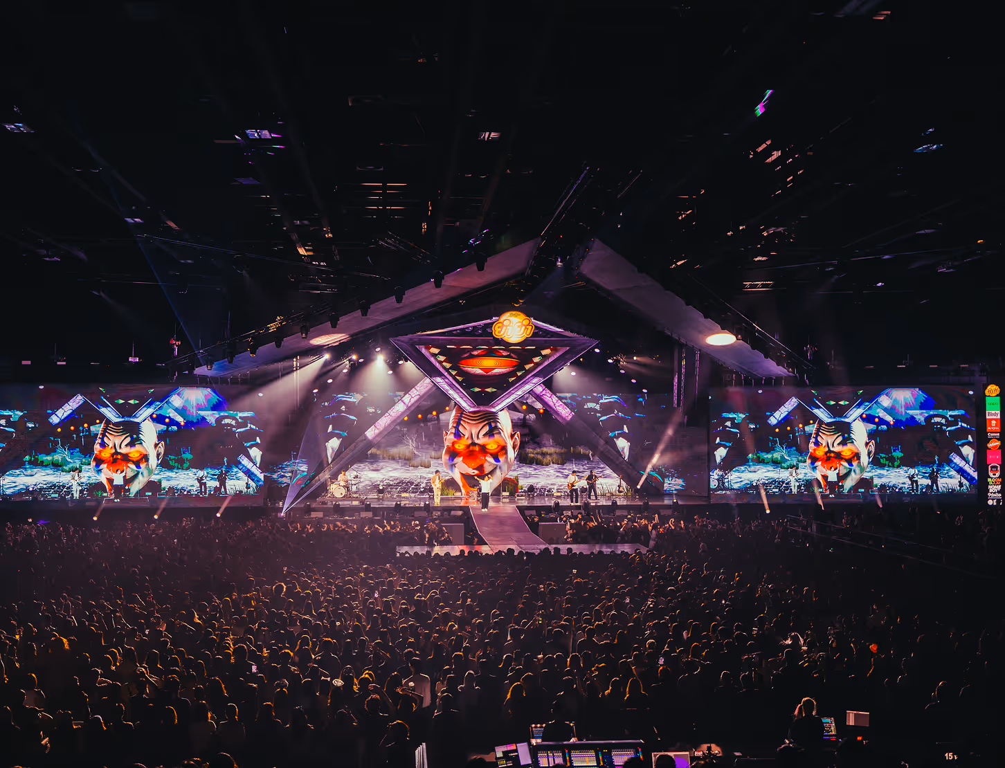 Concert stage with large clown face visuals and crowd watching a live performance indoors.