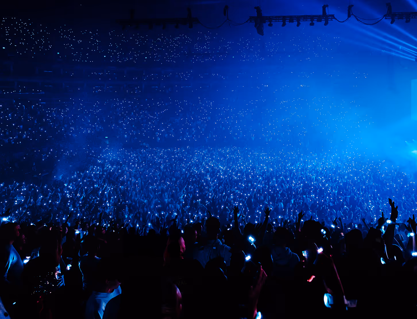 Large crowd at a concert holding blue glowing wristbands lighting up the dark venue.