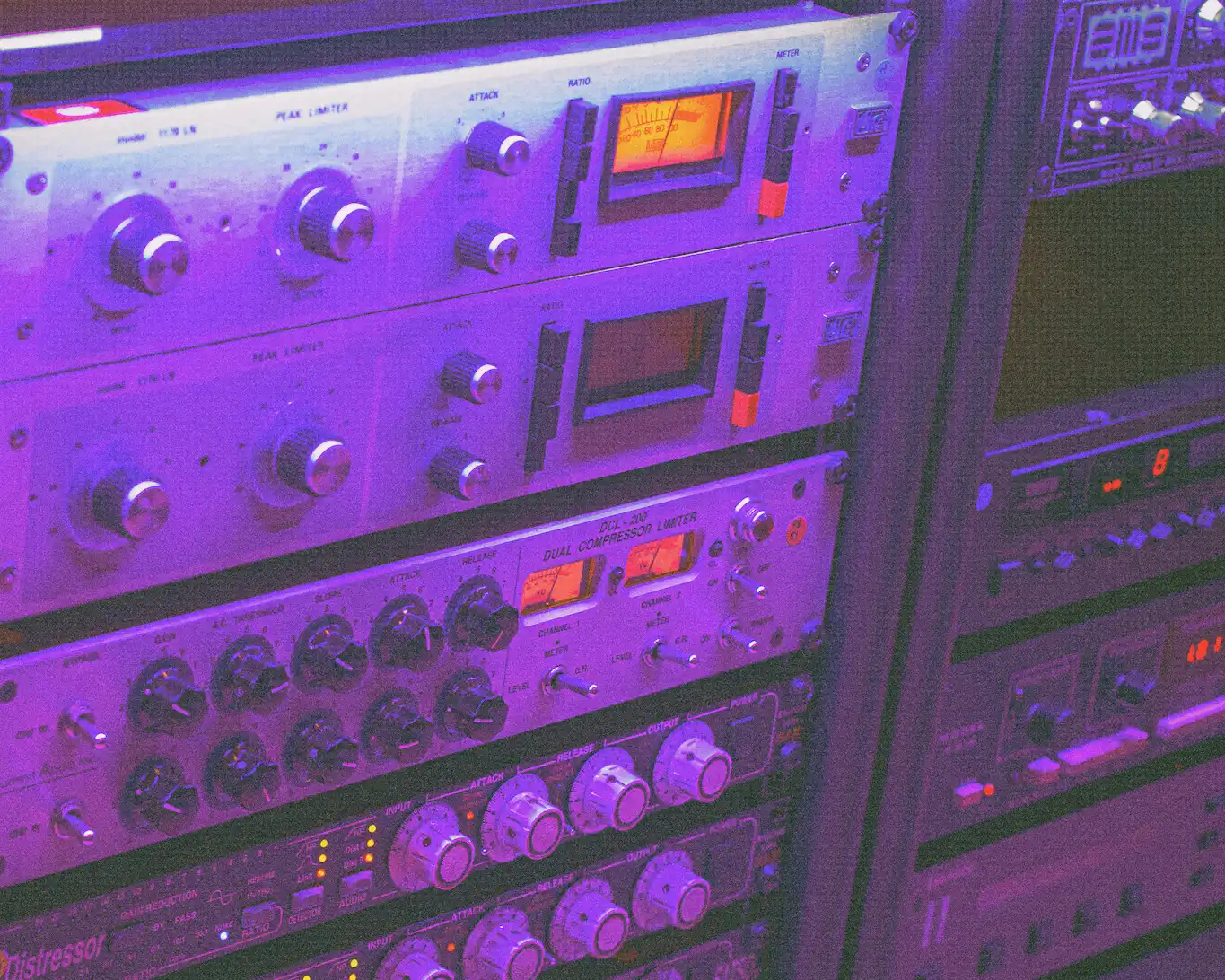 Close-up of audio equipment rack with various knobs, meters, and controls under purple lighting.