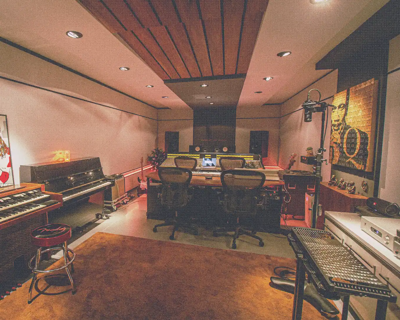 Modern recording studio with mixing console, three office chairs, keyboards, piano, guitars, microphone, and artwork on the wall.