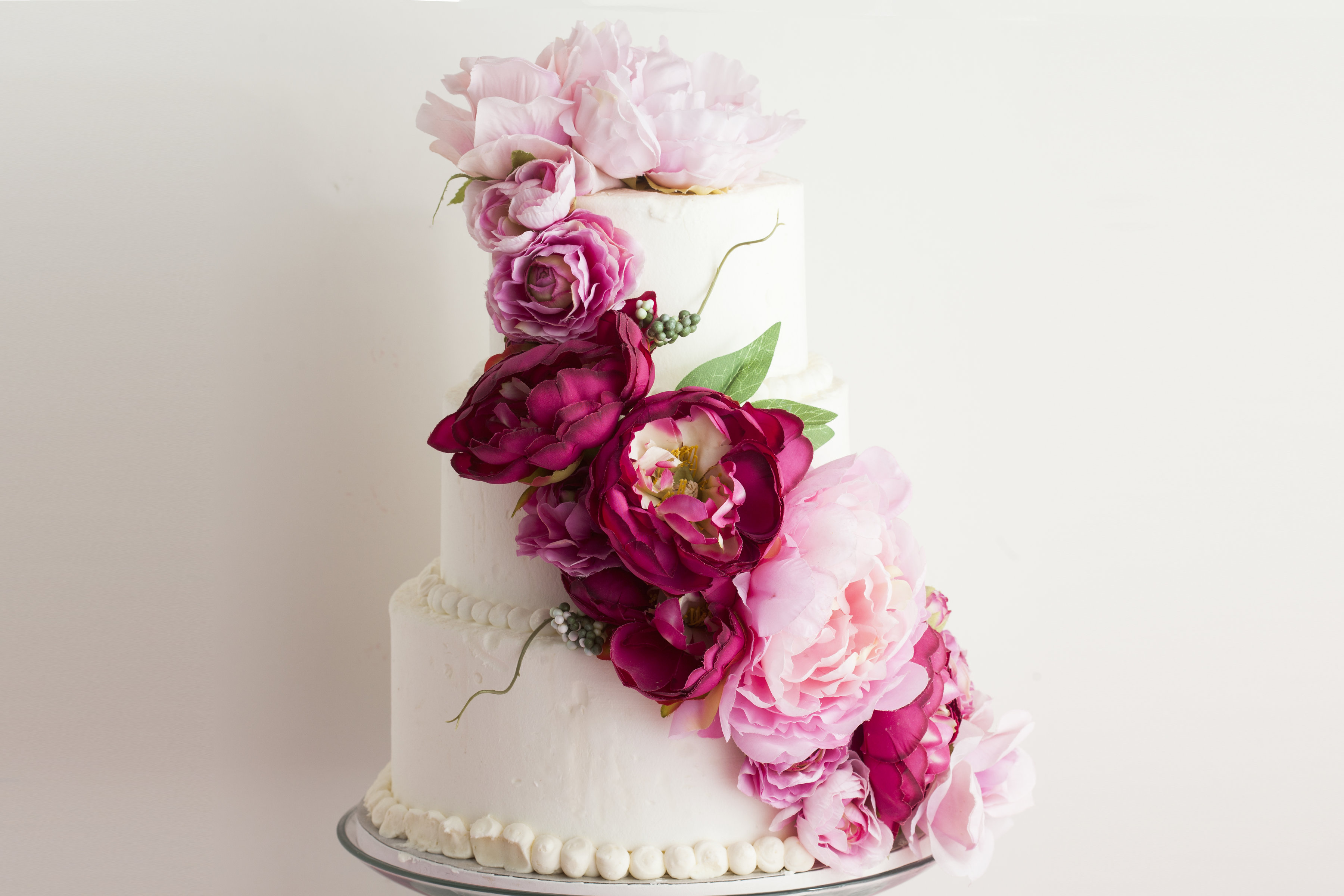 A three tier white wedding cake with pink cascading flowers