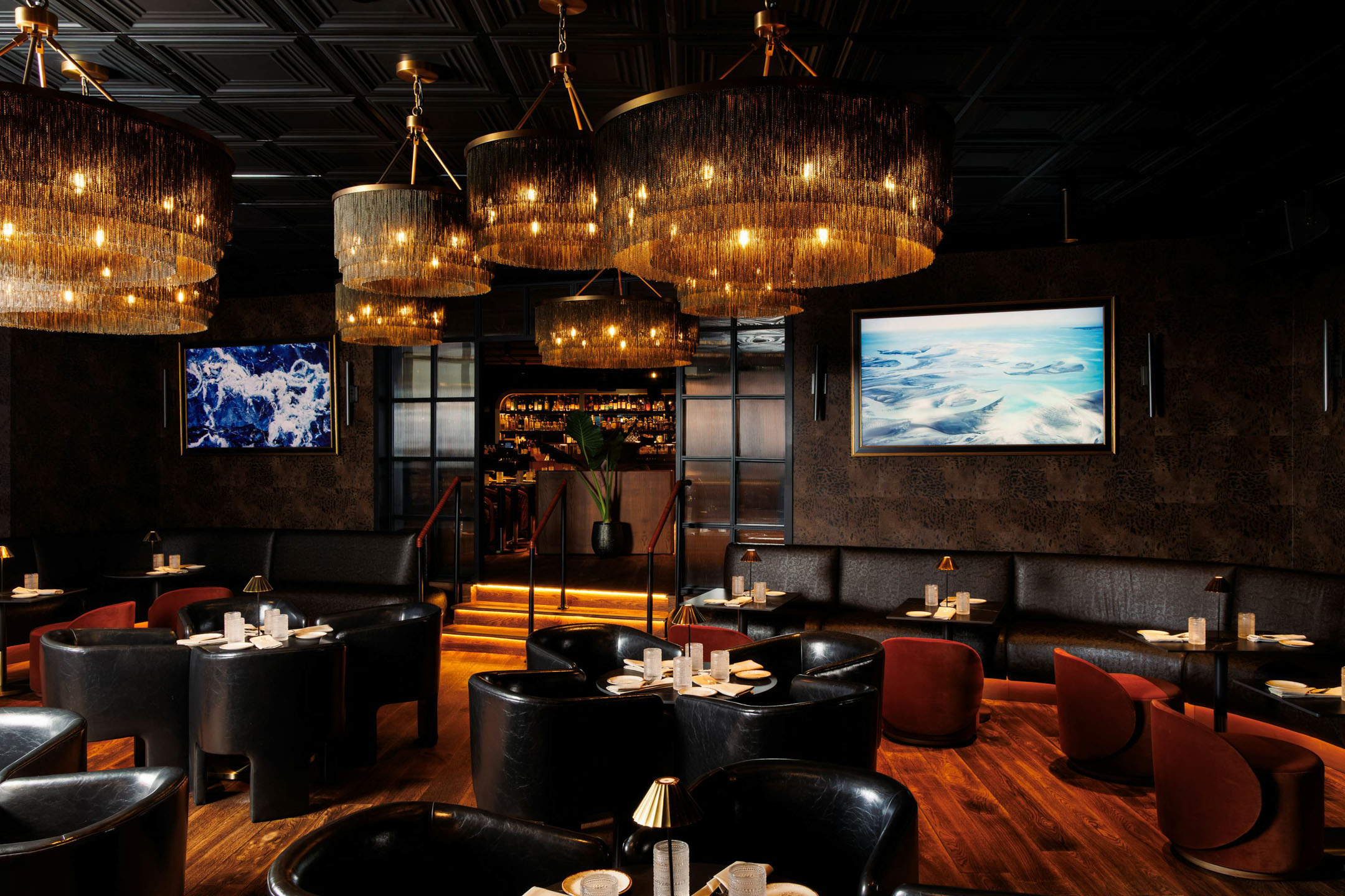 Sophisticated, dimly-lit restaurant interior with plush black seating, elegant chandeliers, and framed artwork. Warm, inviting atmosphere.