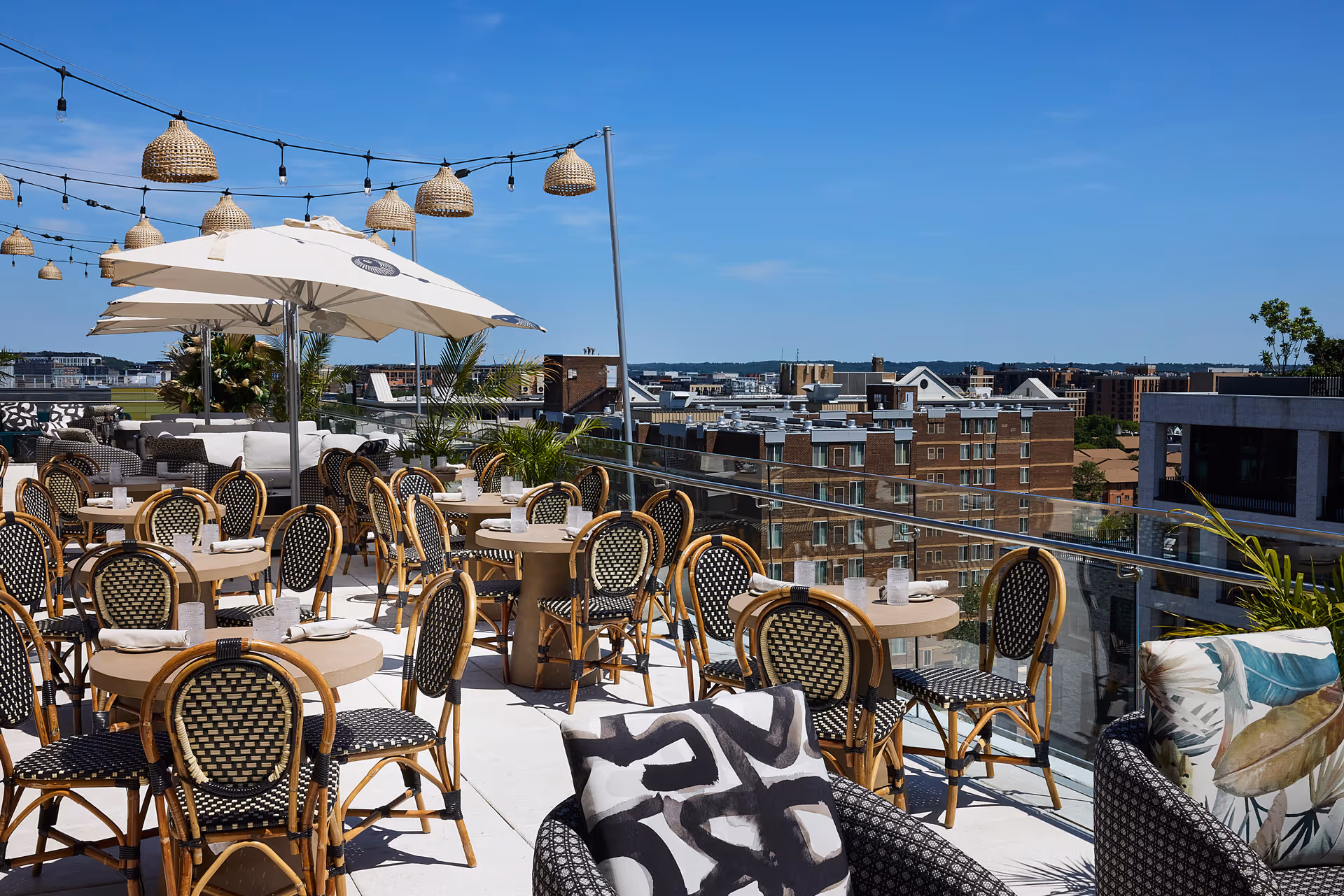 Blue skies and Rooftop views of Washington DC with tables and beige umbrellas and string lights above