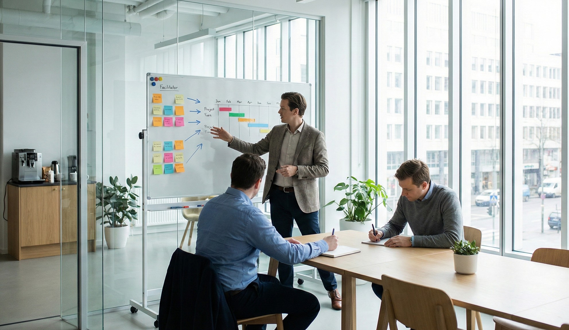 Businessman explaining project timeline on whiteboard with colorful sticky notes while two colleagues take notes in a bright office with large windows.