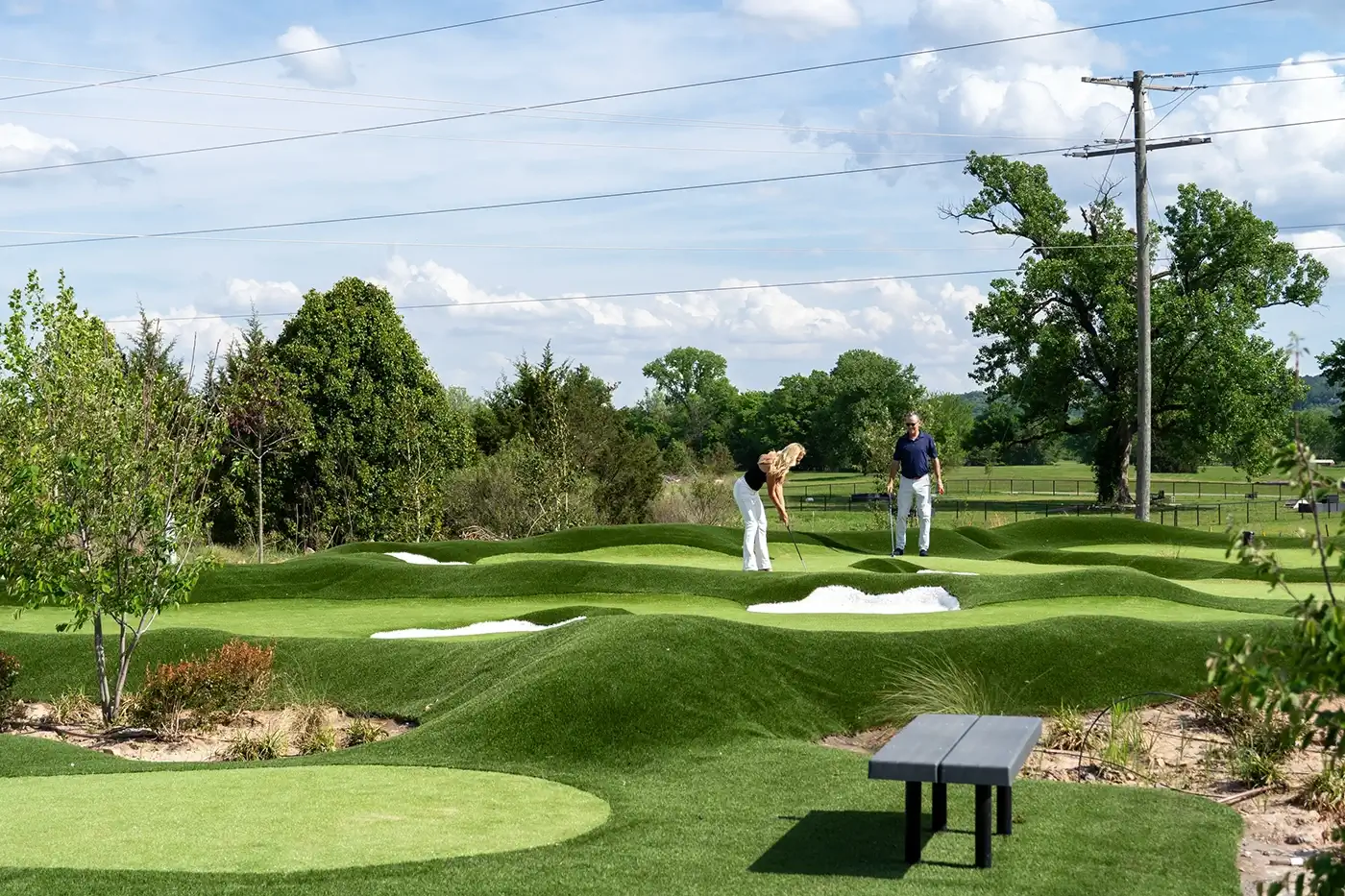 Modern clubhouse at a golf course during twilight with people socializing on the patio and near putting greens.