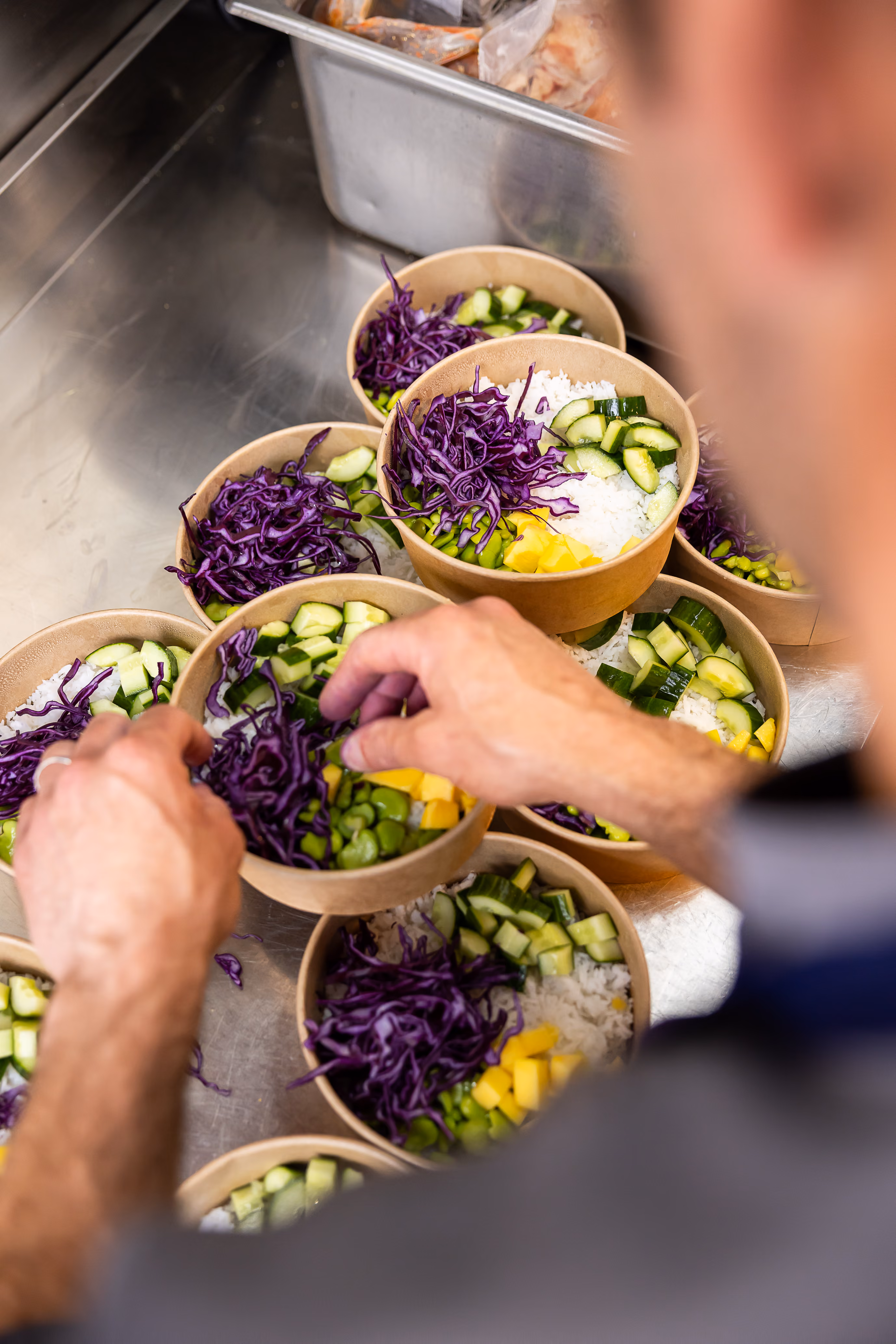 Chef assemblant des poke bowls au riz, chou rouge, concombre, mangue et édamame dans des bols kraft en cuisine