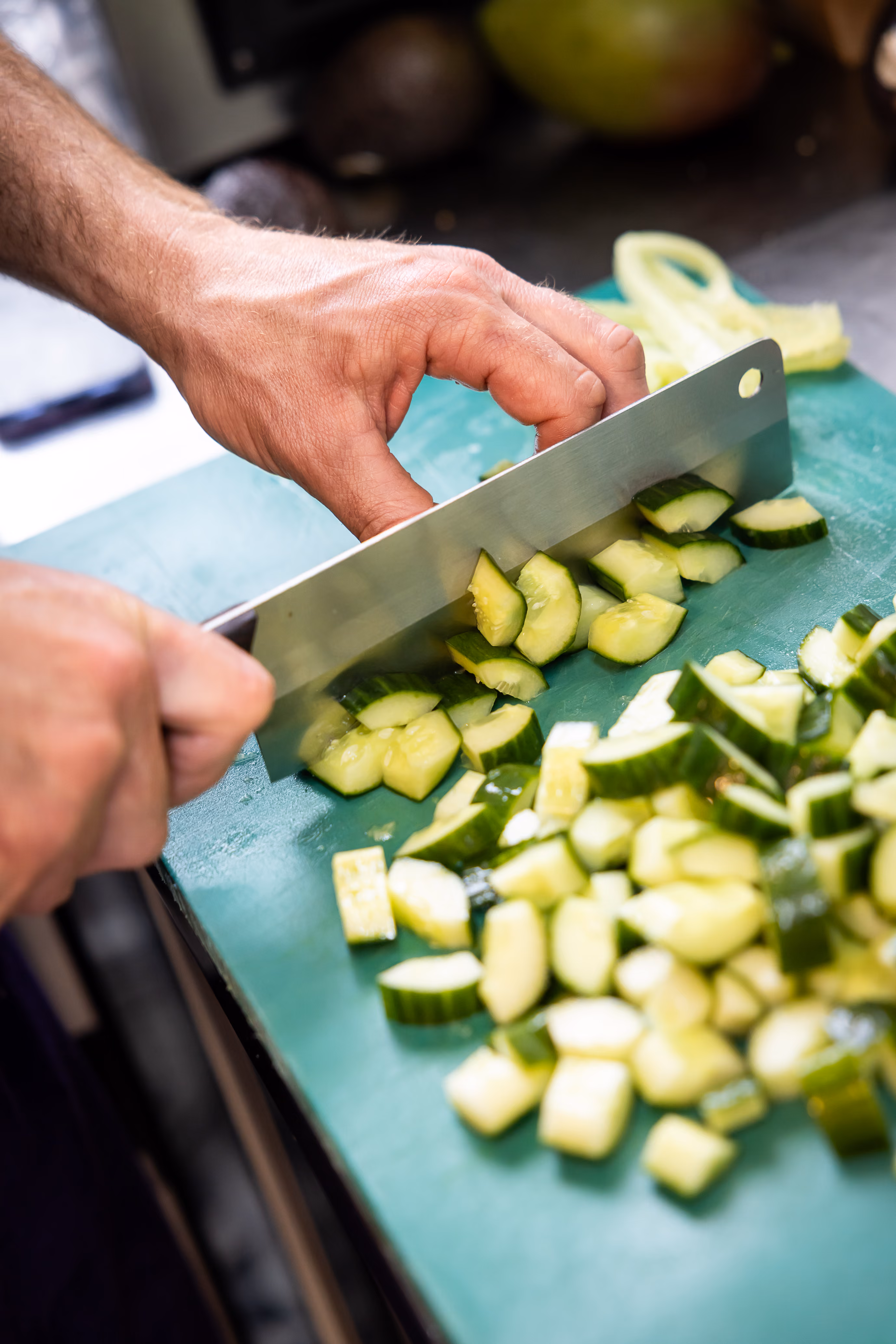 Chef découpant des courgettes en dés au couteau sur une planche verte en cuisine