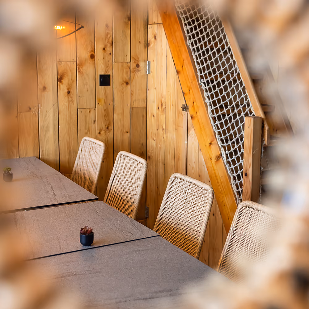 Salle du restaurant : tables en pierre, chaises en rotin et mur en bois clair dans une ambiance chaleureuse