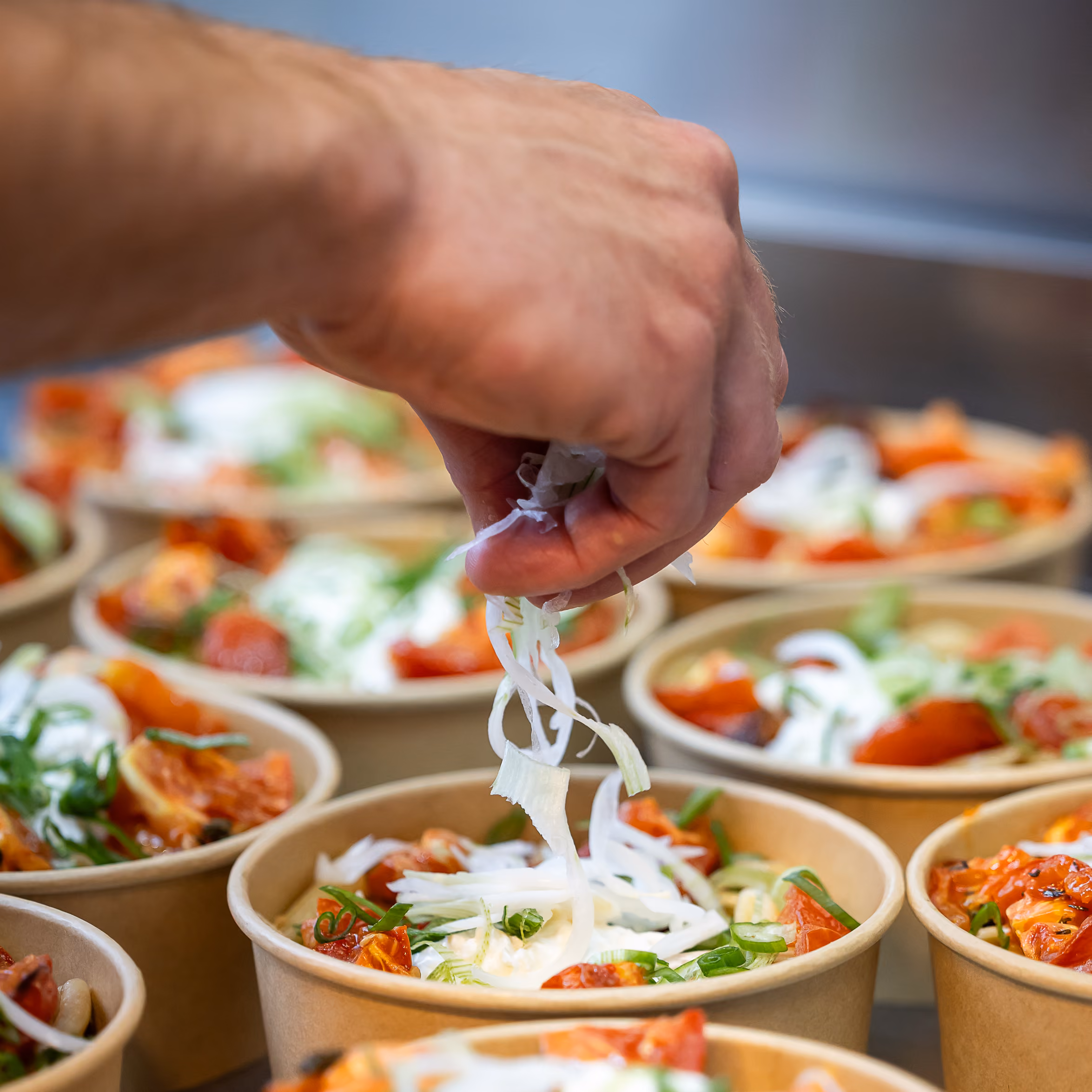 Chef parsemant de l'oignon émincé sur des bols de pâtes aux tomates rôties et ciboule en cuisine