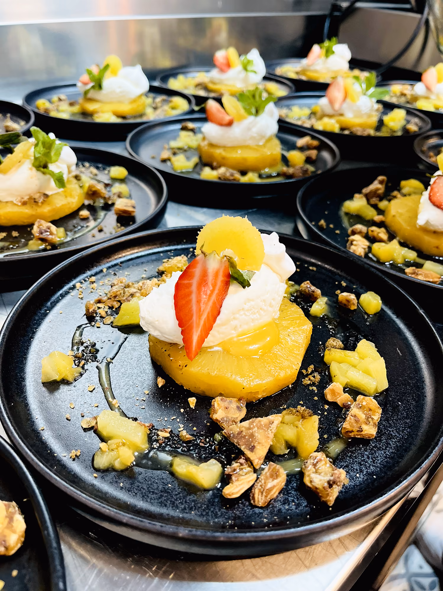 Assiettes dressées d'ananas rôti, crème fouettée, fraise et éclats de nougatine sur assiettes noires