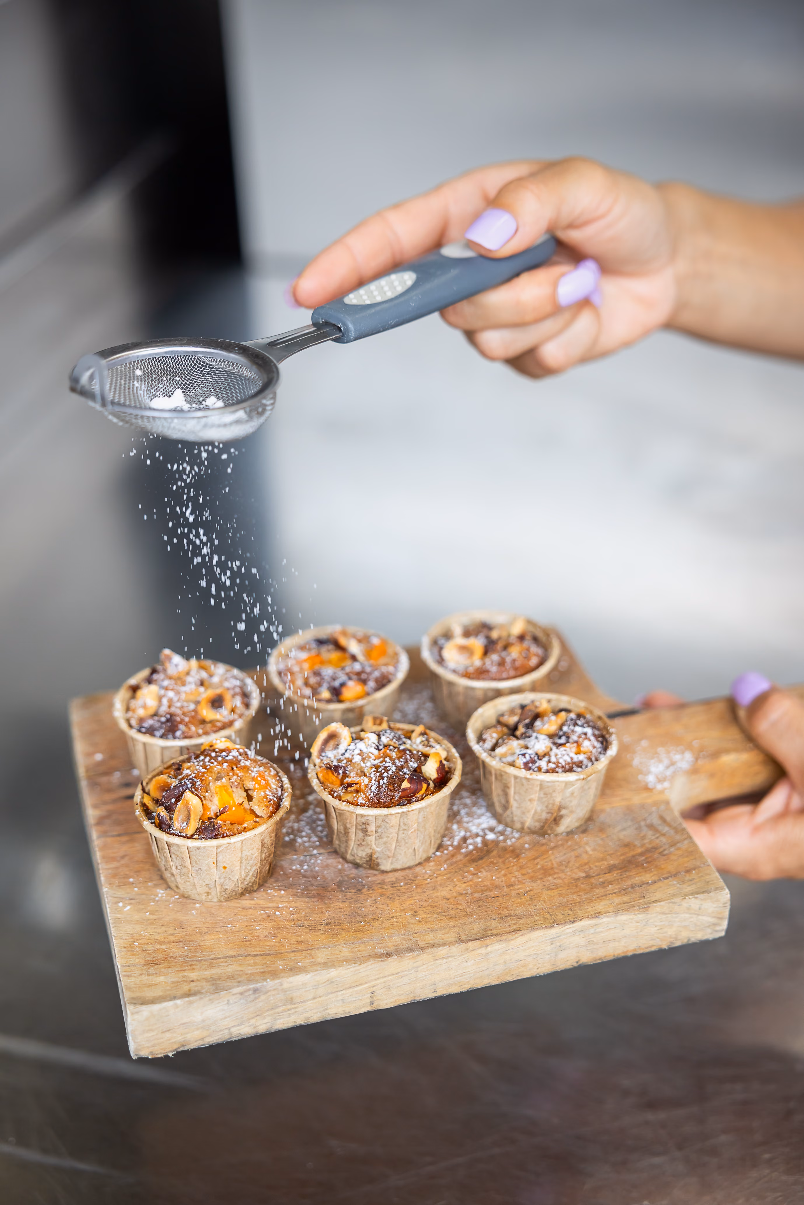 Saupoudrage de sucre glace au tamis sur des mini-crumbles aux noisettes, chocolat et abricot sur planche en bois