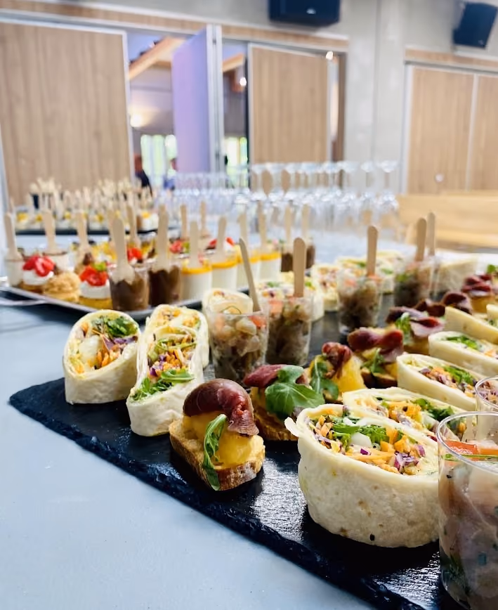 Buffet traiteur dressé en salle de réception : wraps, canapés, verrines et cuillères apéritives sur ardoise