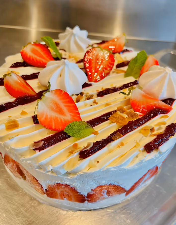 Entremets aux fraises et crème fouettée, décoré de meringues, coulis de fruits rouges, amandes et menthe