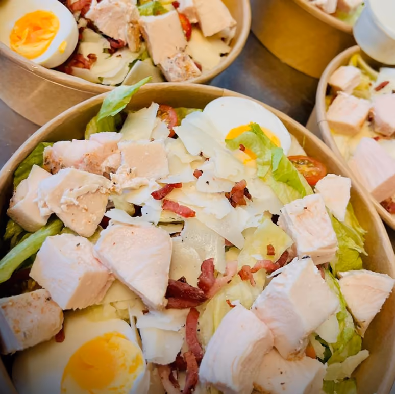 Salades César au poulet, œuf, copeaux de parmesan, lardons et tomate en bols kraft