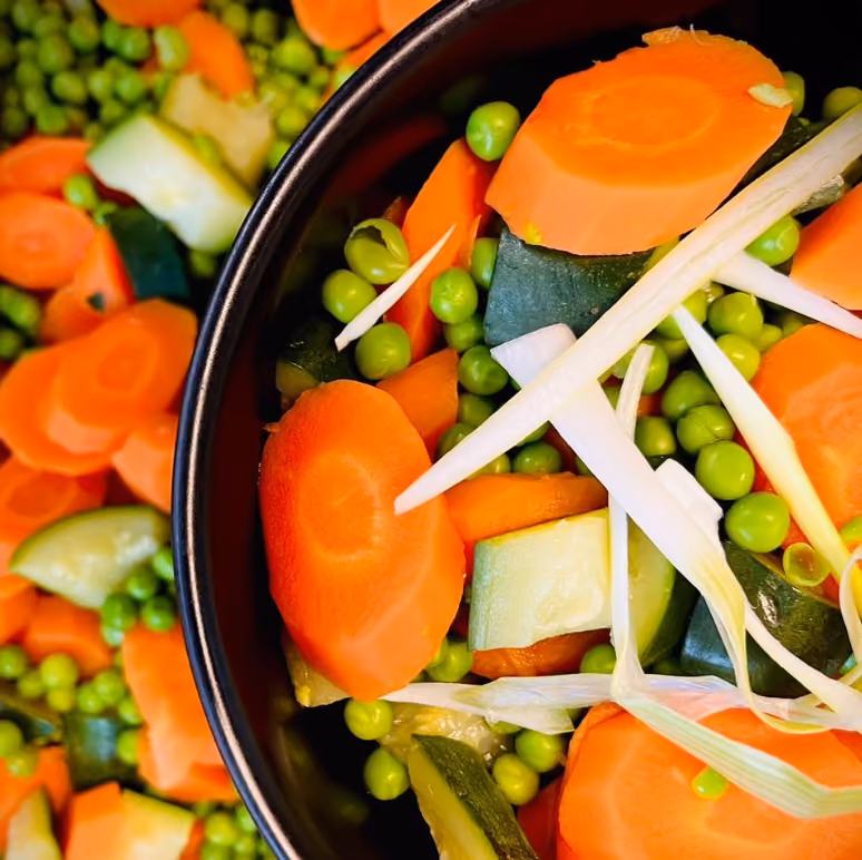 Poêlée de légumes frais : carottes, petits pois, courgettes et oignon émincé dans un bol noir