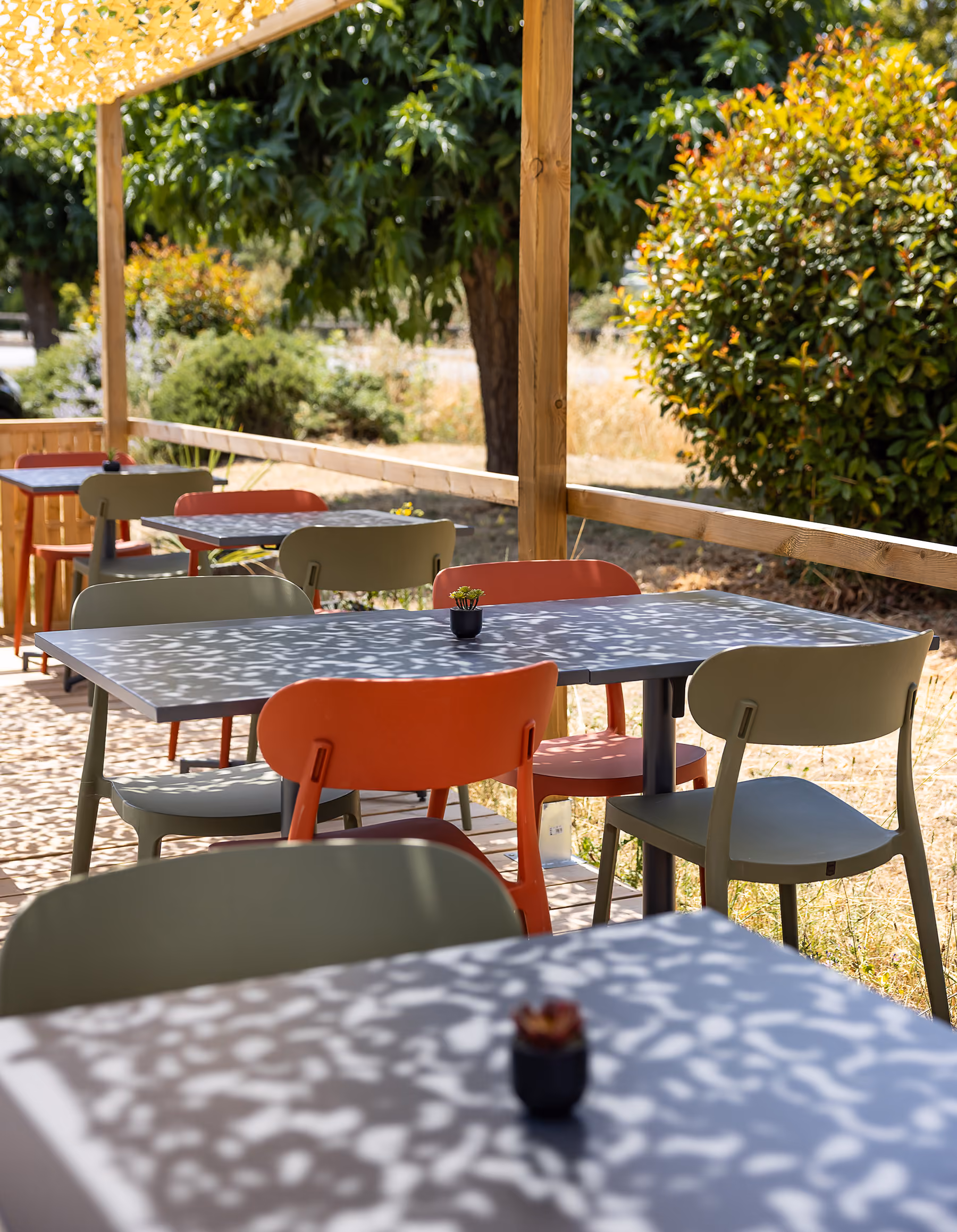 Terrasse ombragée du restaurant avec tables et chaises colorées vertes et orange sous une pergola en bois