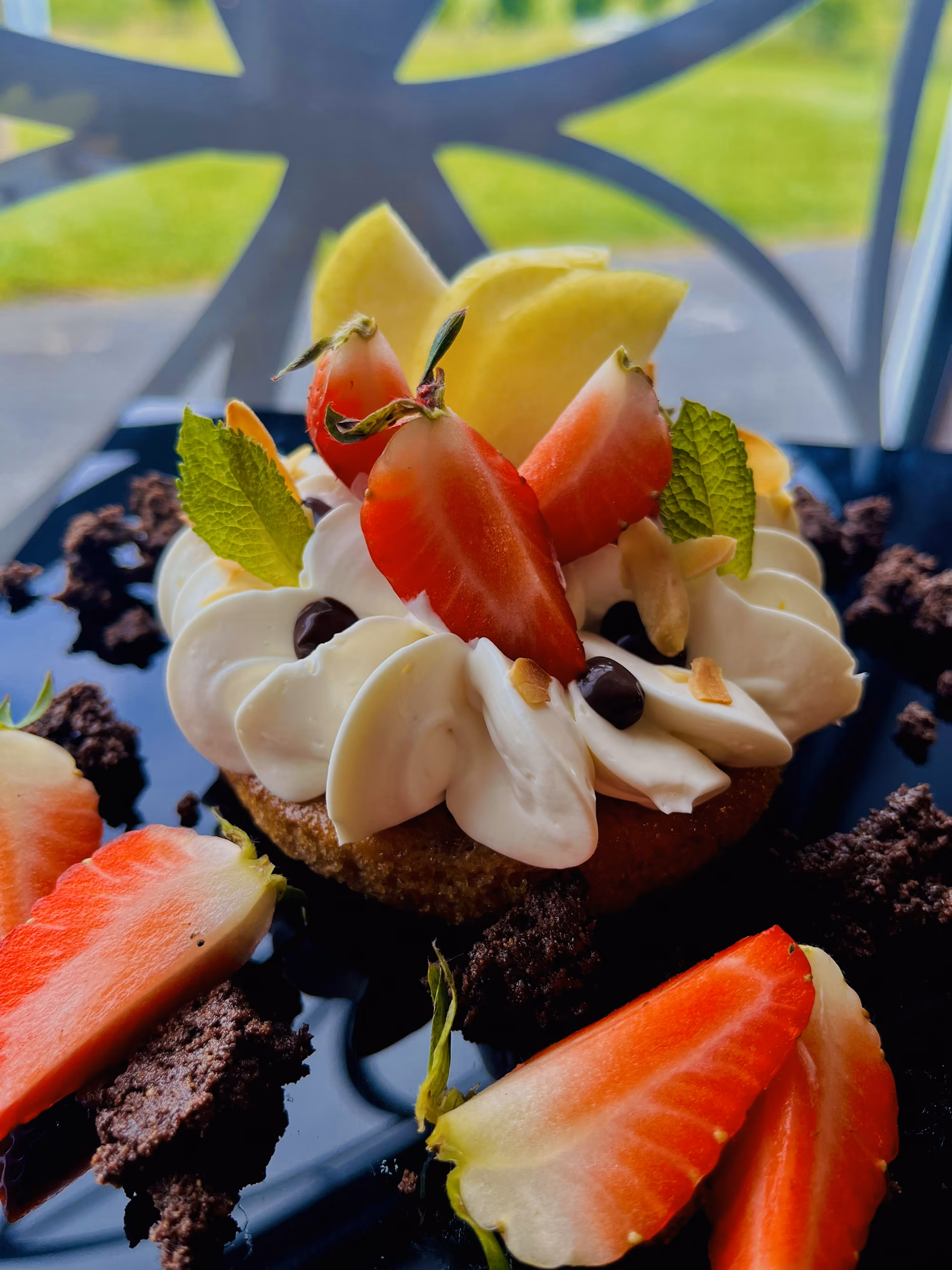 Tartelette à la crème fouettée, fraises fraîches, pépites de chocolat et menthe, dressée sur table extérieure