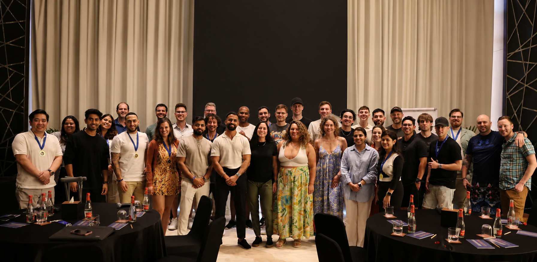 Group photo of 30 diverse adults standing in a conference room with tables and a screen that reads Decentralized Masters.