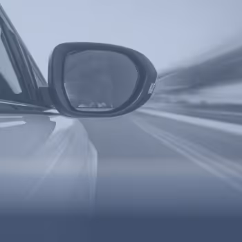 Seitenspiegel eines Autos mit unscharfer Straße im Hintergrund in Bewegungsunschärfe.