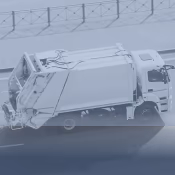 Ein Müllwagen fährt auf einer Straßenbahnlinie neben einem Gehweg mit Geländer.