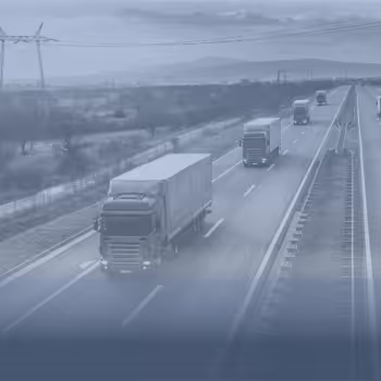 Mehrere Lastwagen fahren auf einer leeren Autobahn mit Stromleitungen und Bergen im Hintergrund.