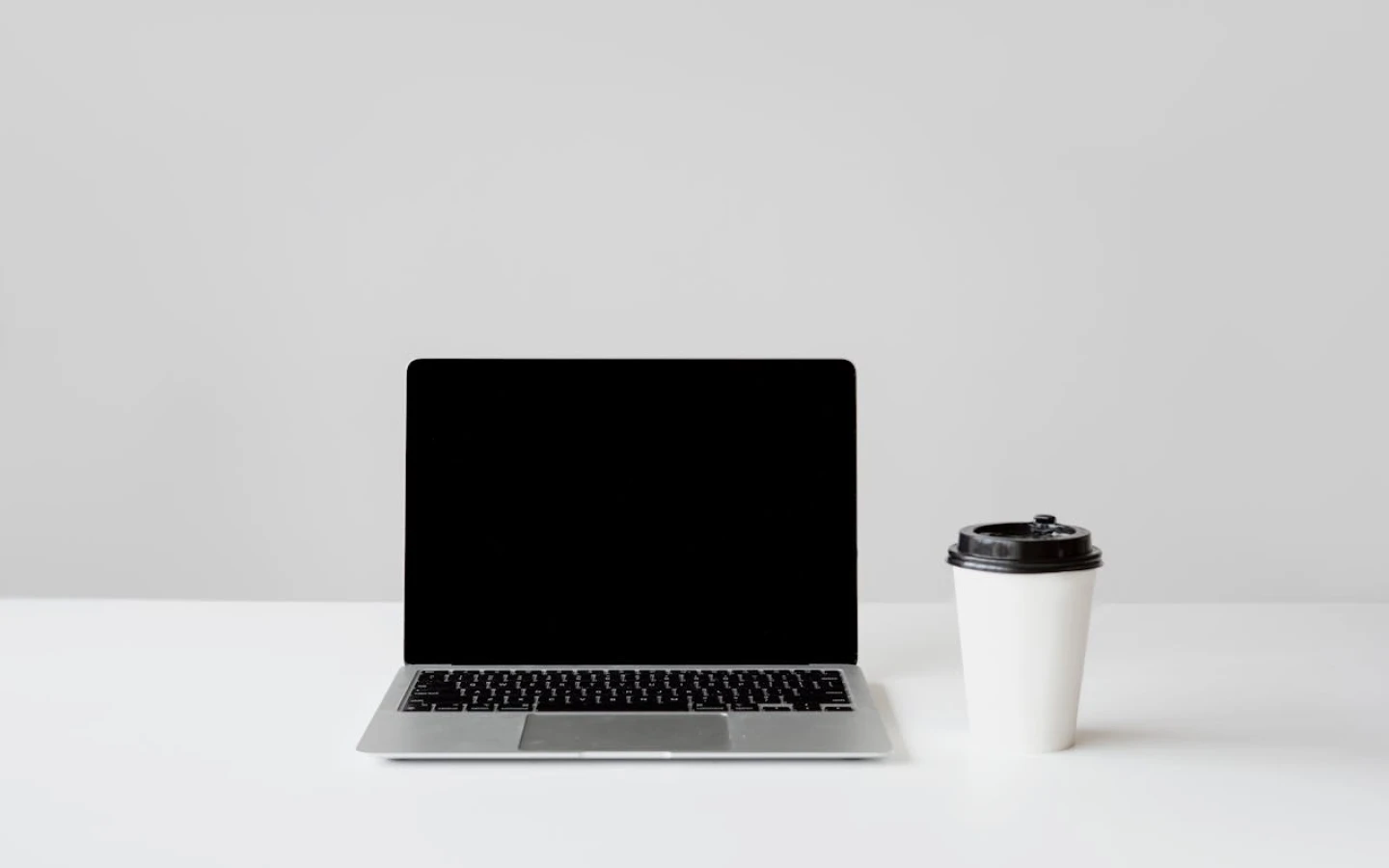 Minimal workspace setup with a laptop and a coffee cup on a clean white desk.