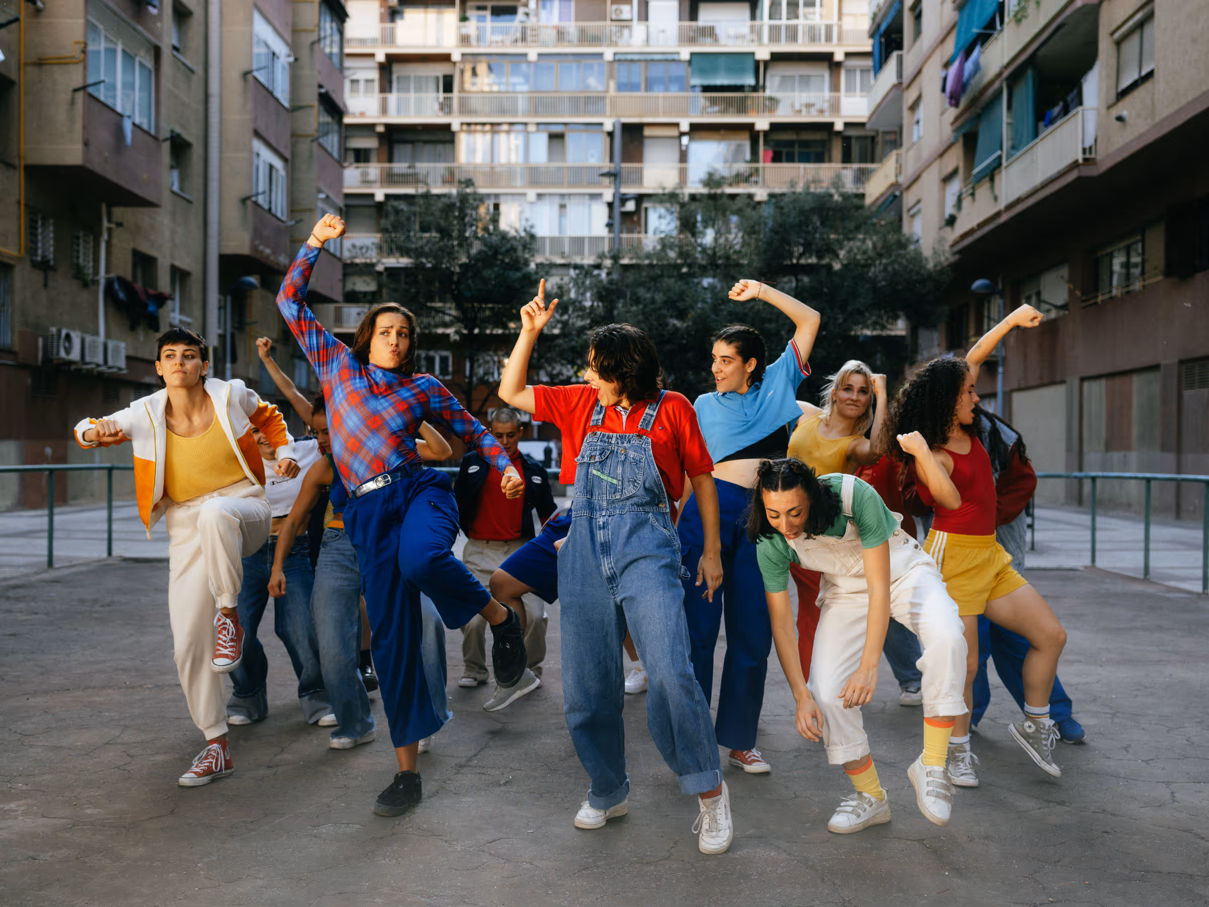 Group of diverse young people dancing energetically outdoors in an urban courtyard surrounded by apartment buildings.