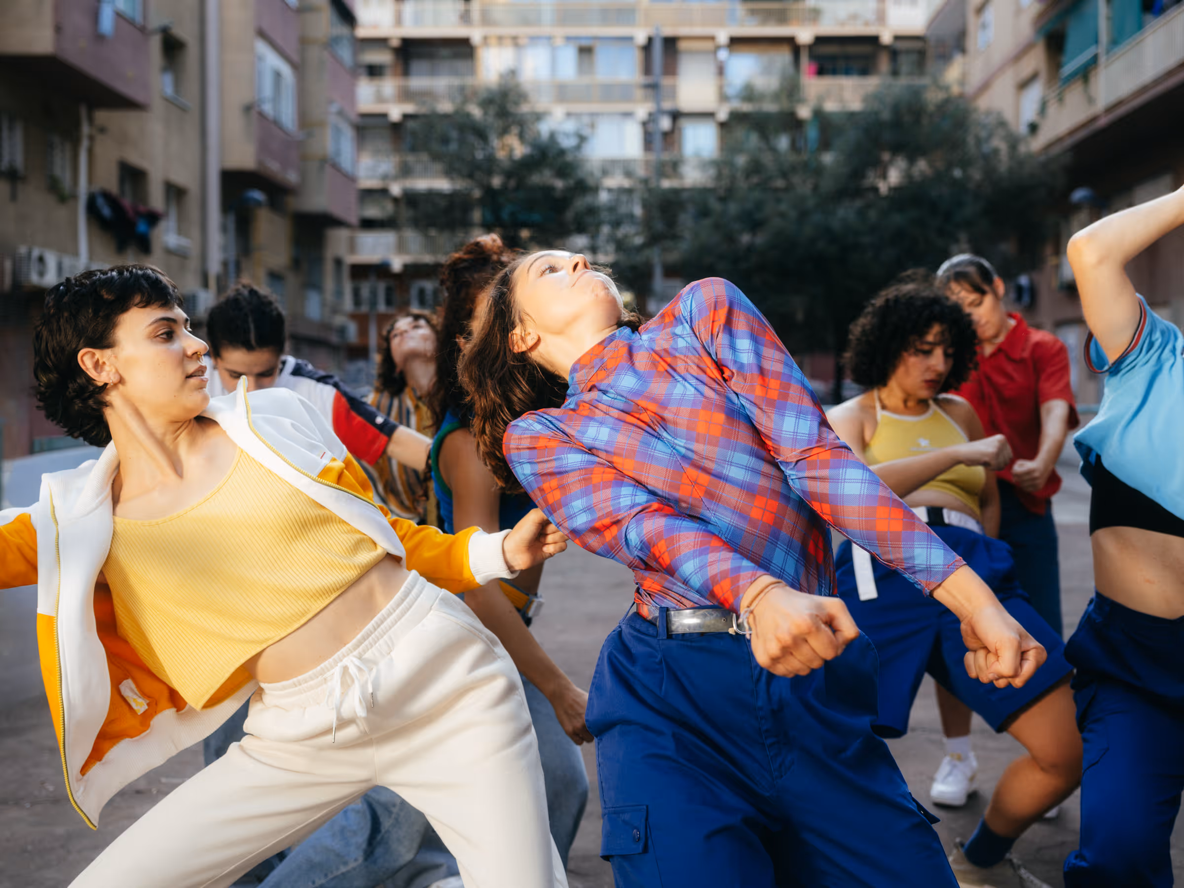 Group of diverse young people dancing energetically in an urban outdoor setting with buildings in the background.