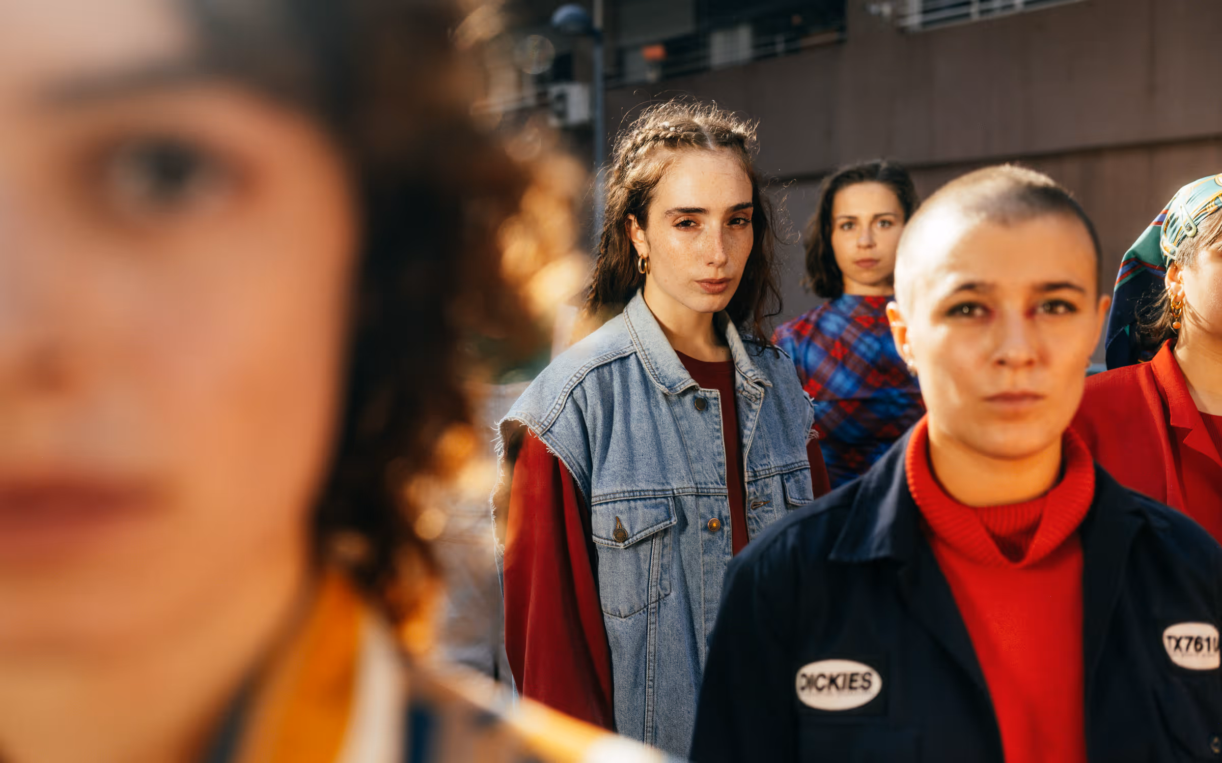 Group of five young adults standing outdoors with serious expressions, two in foreground and three in background.