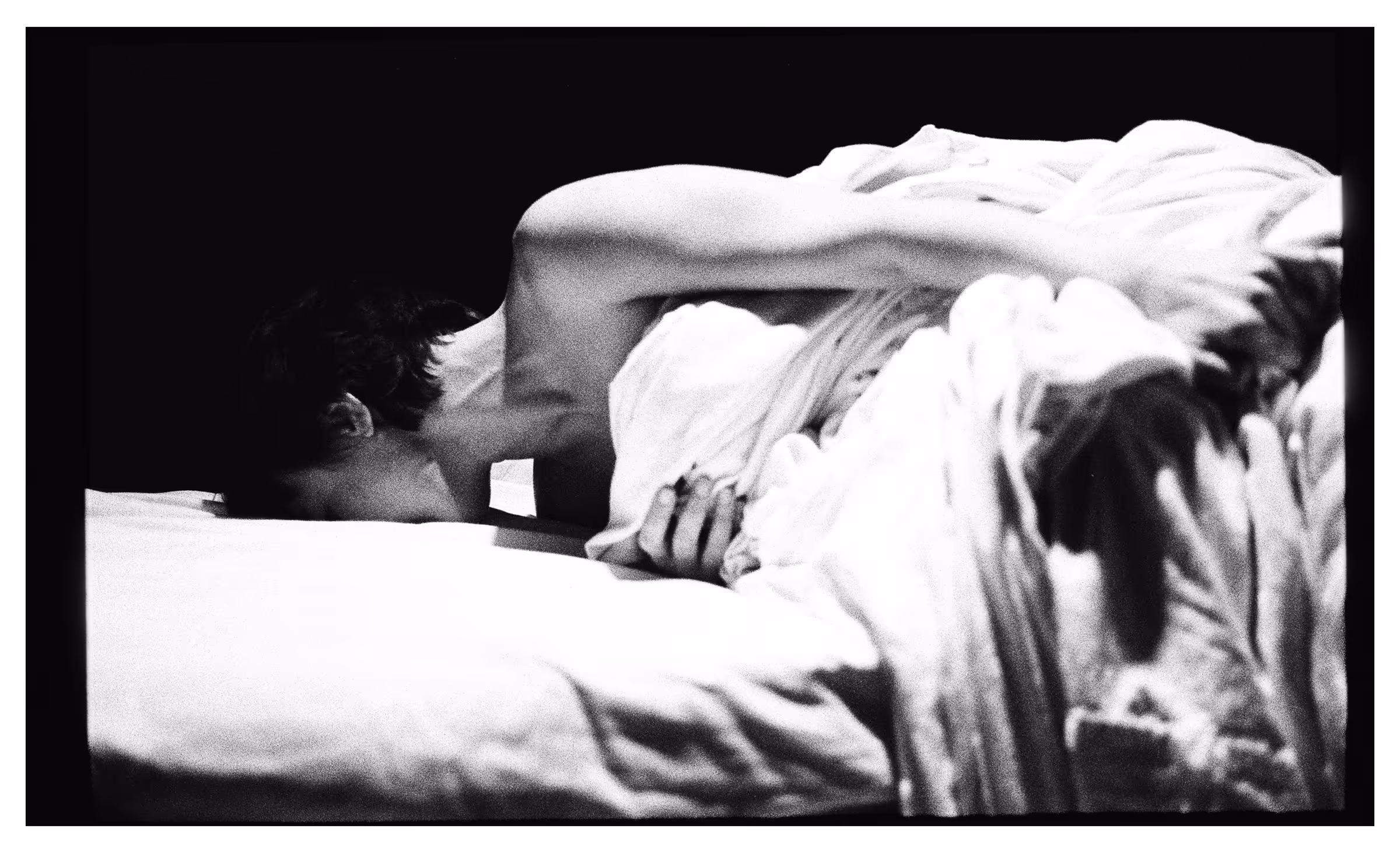 Black and white photo of a person lying face down on a bed, partially covered by a blanket.