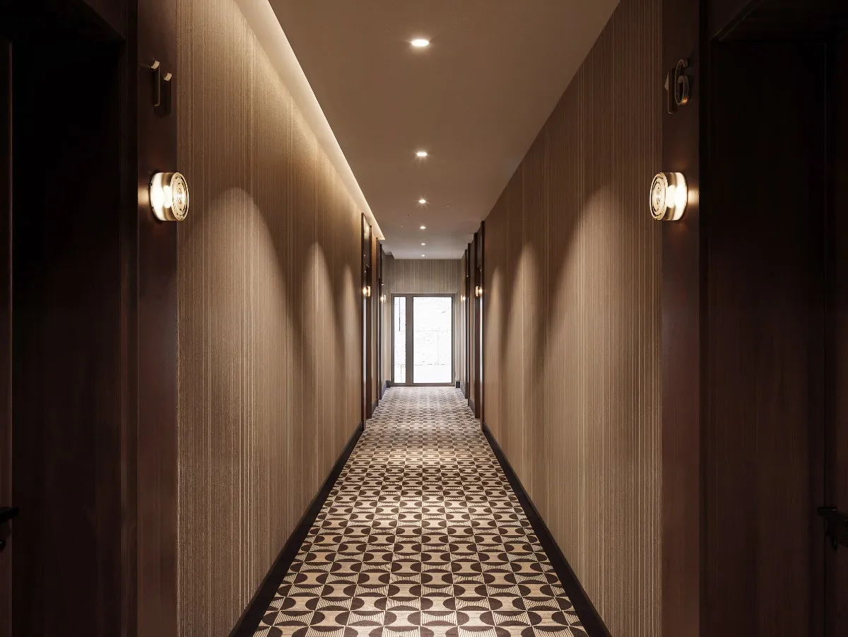 Elegancki hotelowy korytarz z geometrycznym wzorem na dywanie i ciepłym oświetleniem ściennym.