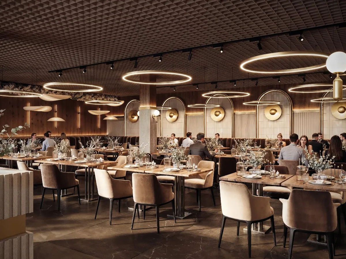Elegancka sala bankietowa z nowoczesnymi okrągłymi lampami sufitowymi, drewnianymi stołami i beżowymi krzesłami, z gośćmi siedzącymi przy stolikach.