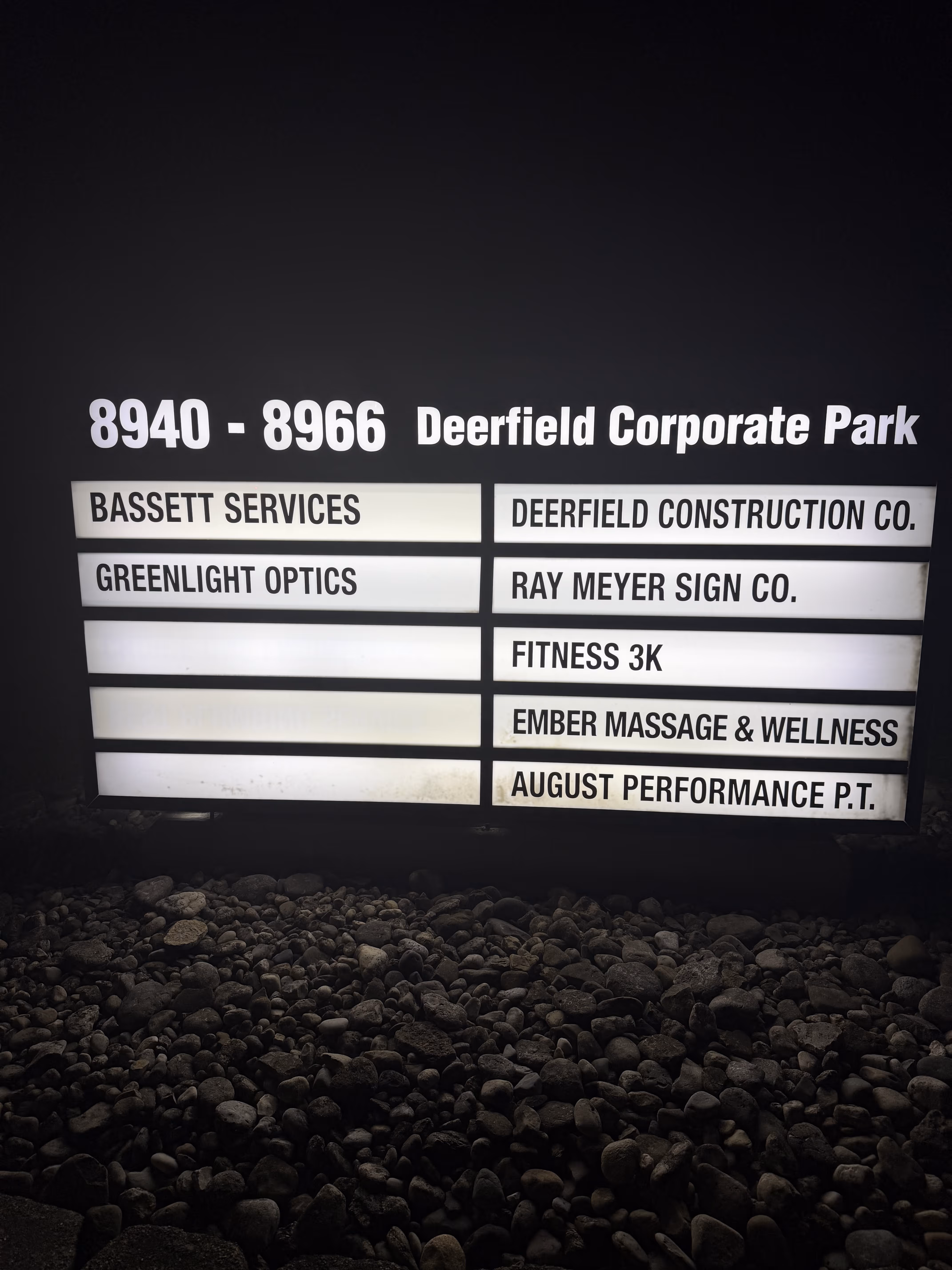 Illuminated directory sign for 8940 - 8966 Deerfield Corporate Park listing businesses including Bassett Services, Greenlight Optics, Deerfield Construction Co., Ray Meyer Sign Co., Fitness 3K, Ember Massage & Wellness, and August Performance P.T.