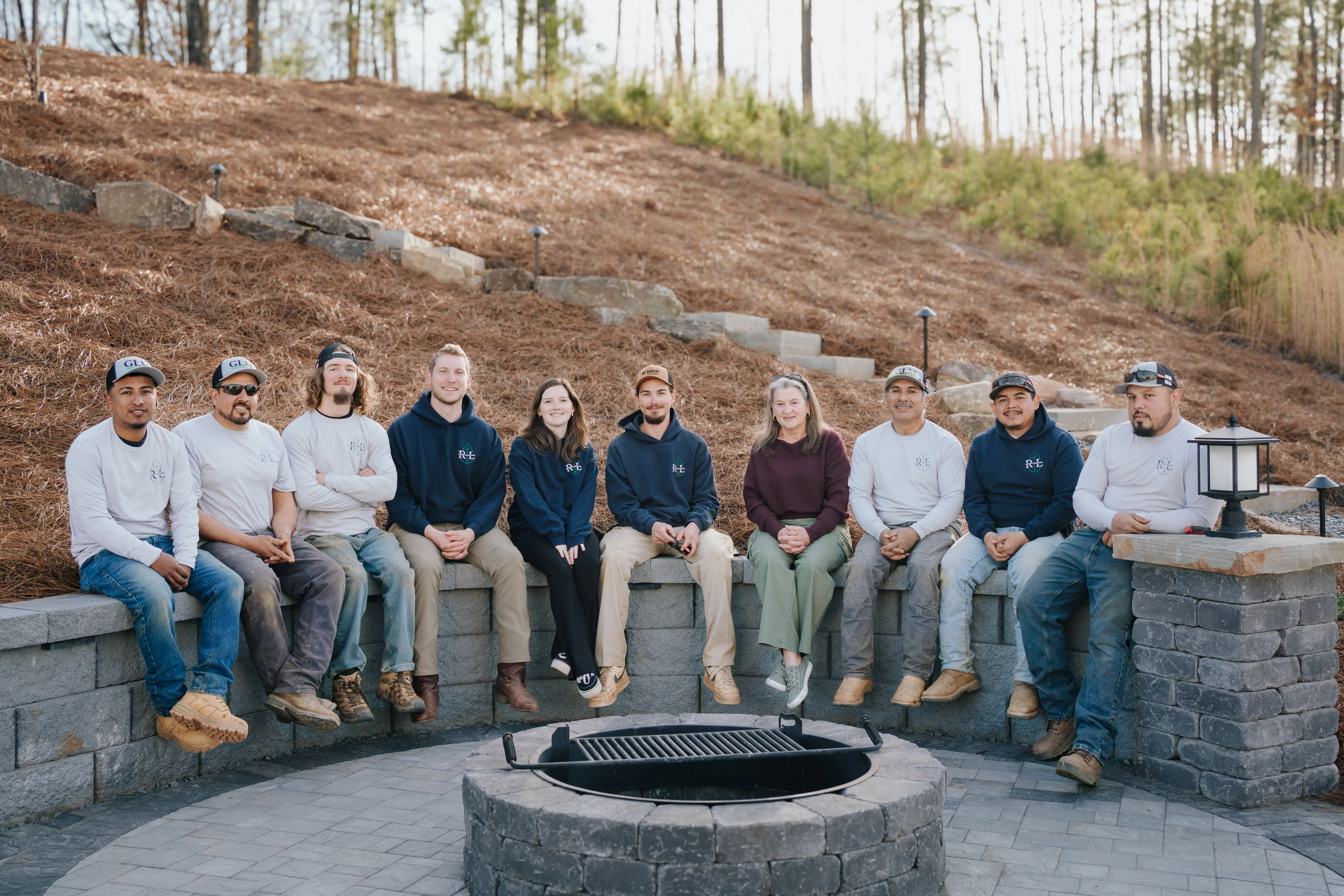 Rooted team sitting with client on retaining wall behind paver patio and fire pit