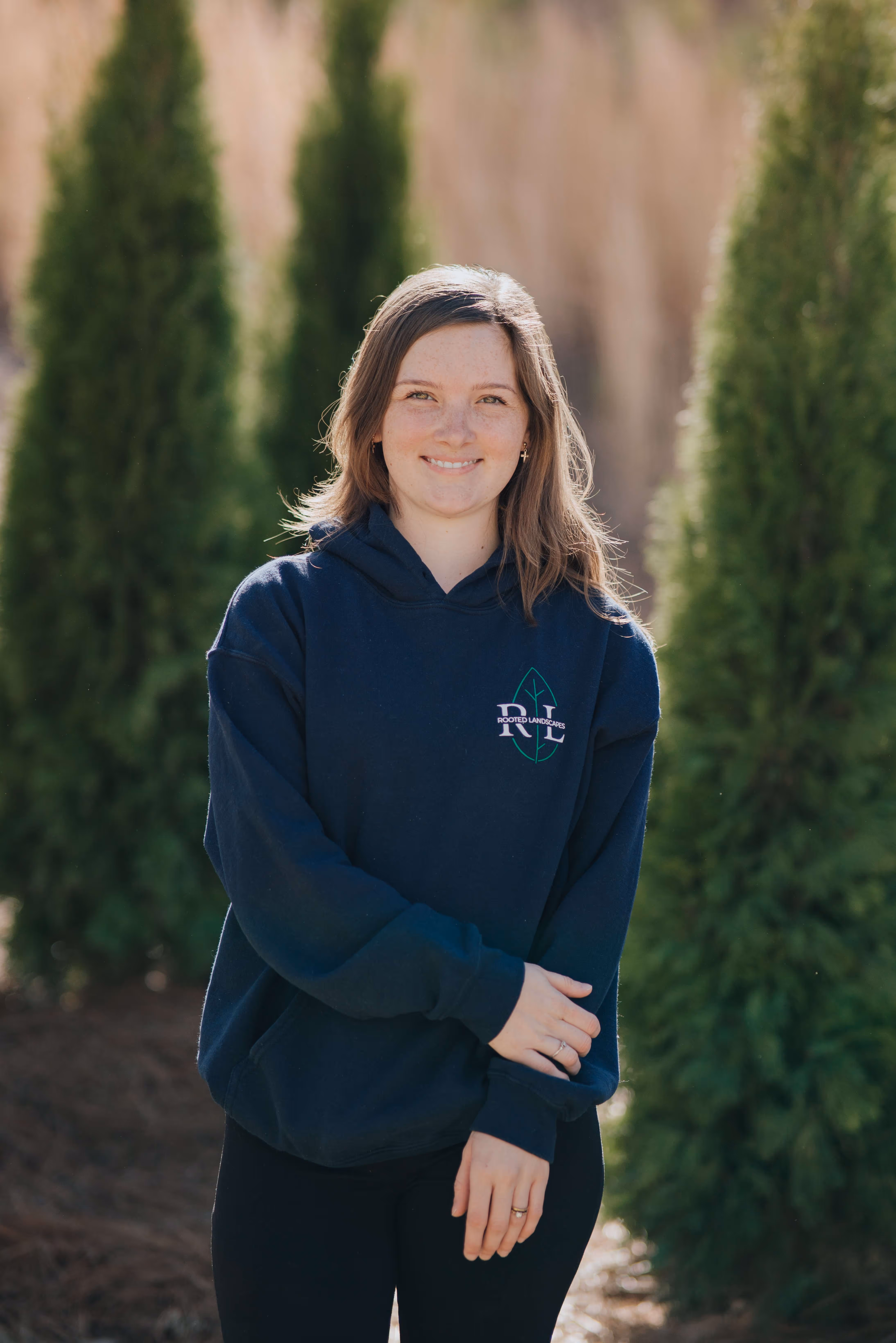 photo of woman in blue sweatshirt smiling with trees in background