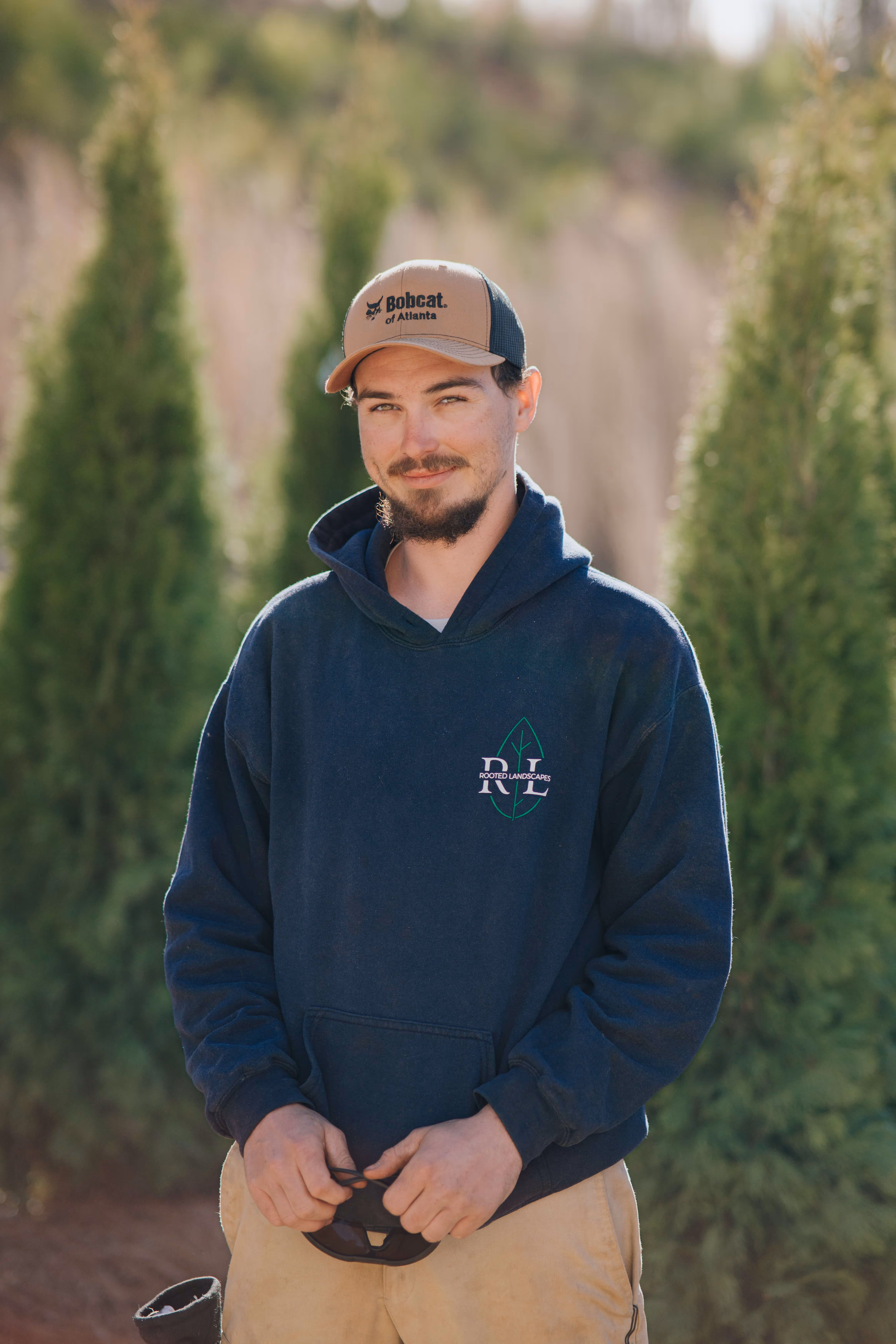 photo of man in blue sweatshirt smiling with trees in background