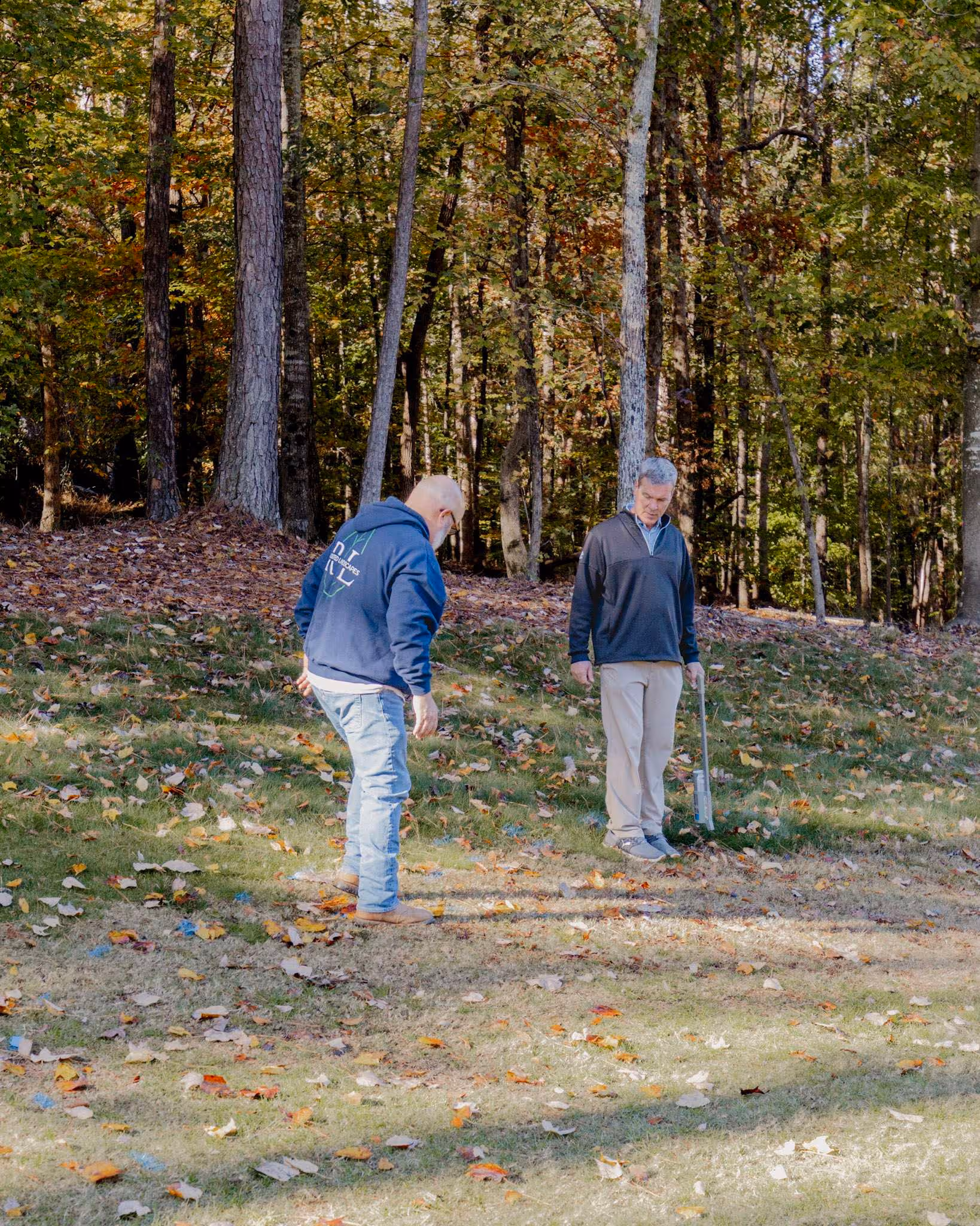 photo of 2 men surveying land in grassy area with trees in background
