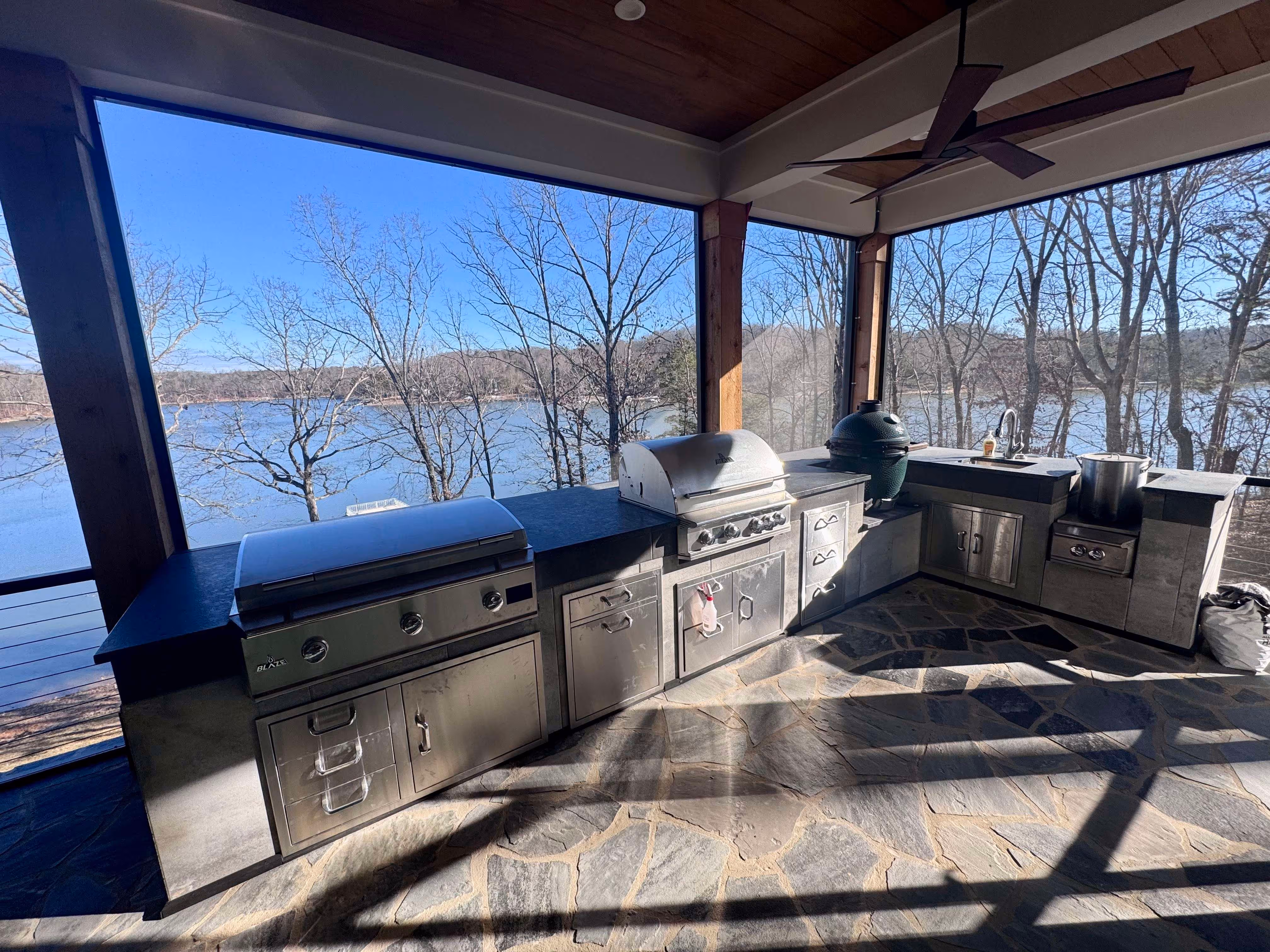 flagstone patio in outdoor kitchen with grill and appliances overlooking lake background