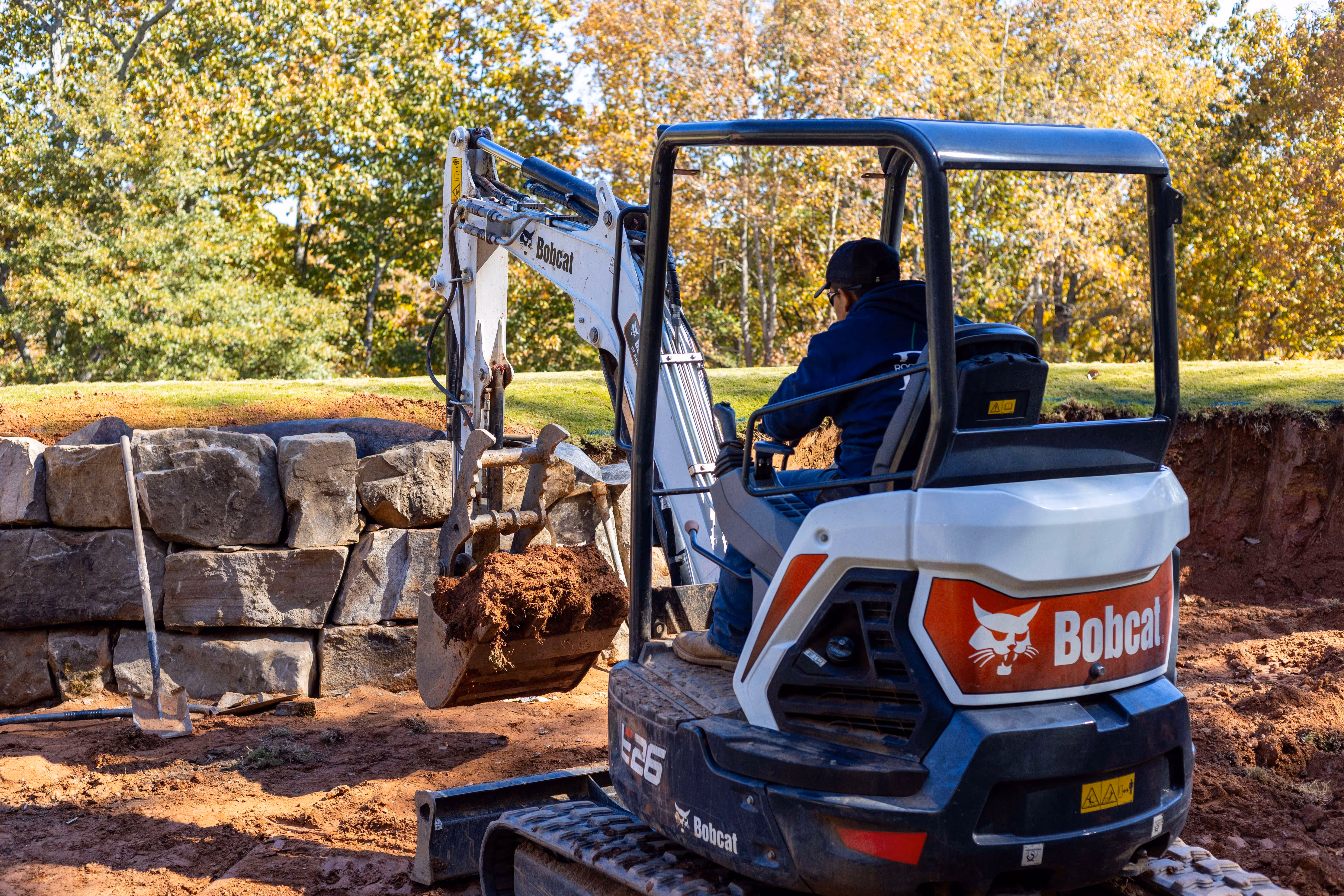 Worker moving dirt on Bobcat equipment in front of boulder wall