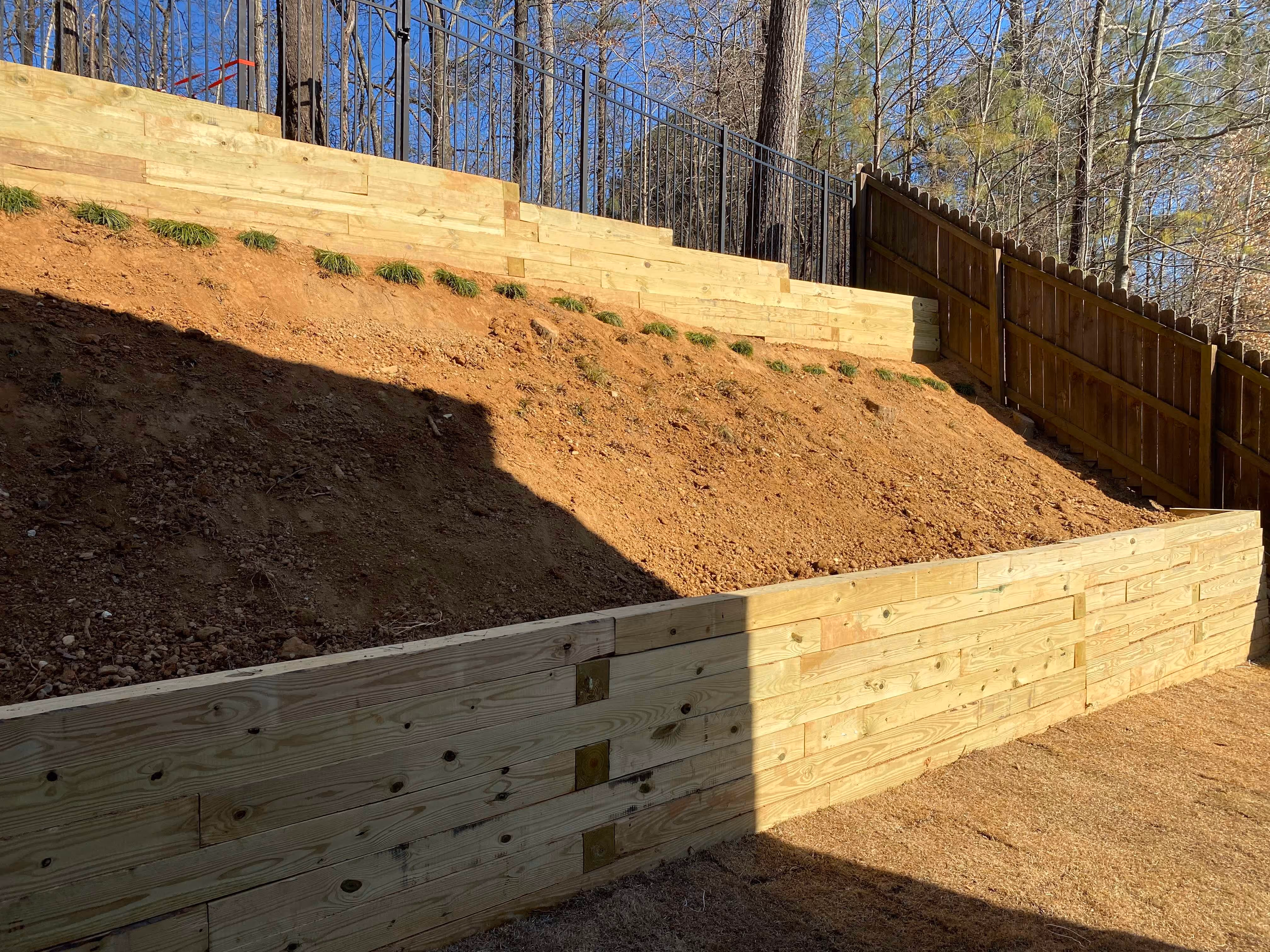 two layered timber retaining wall in back yard with dirt on each level and fence in background